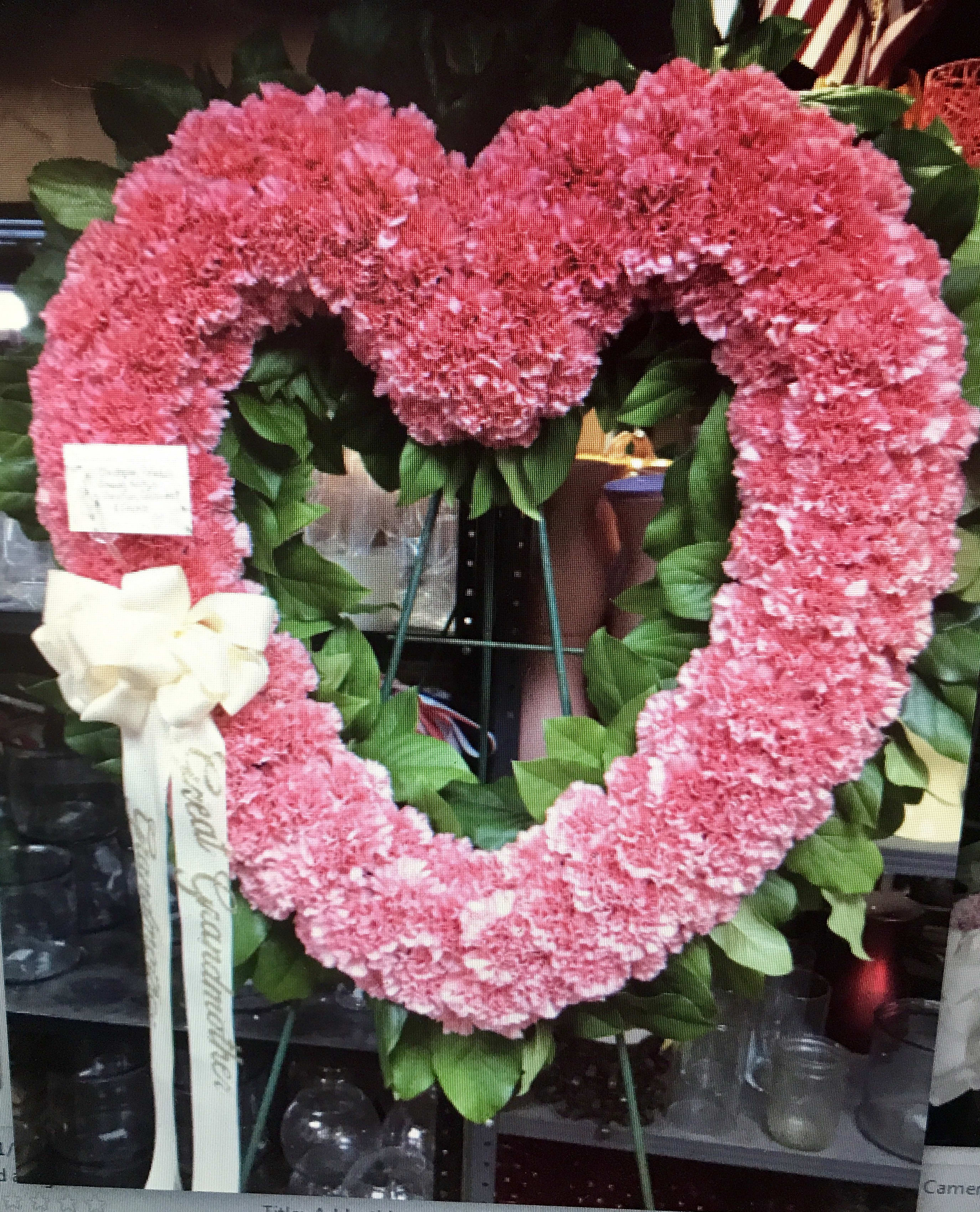 Pink heart-shaped floral wreath on an easel with a white ribbon bow