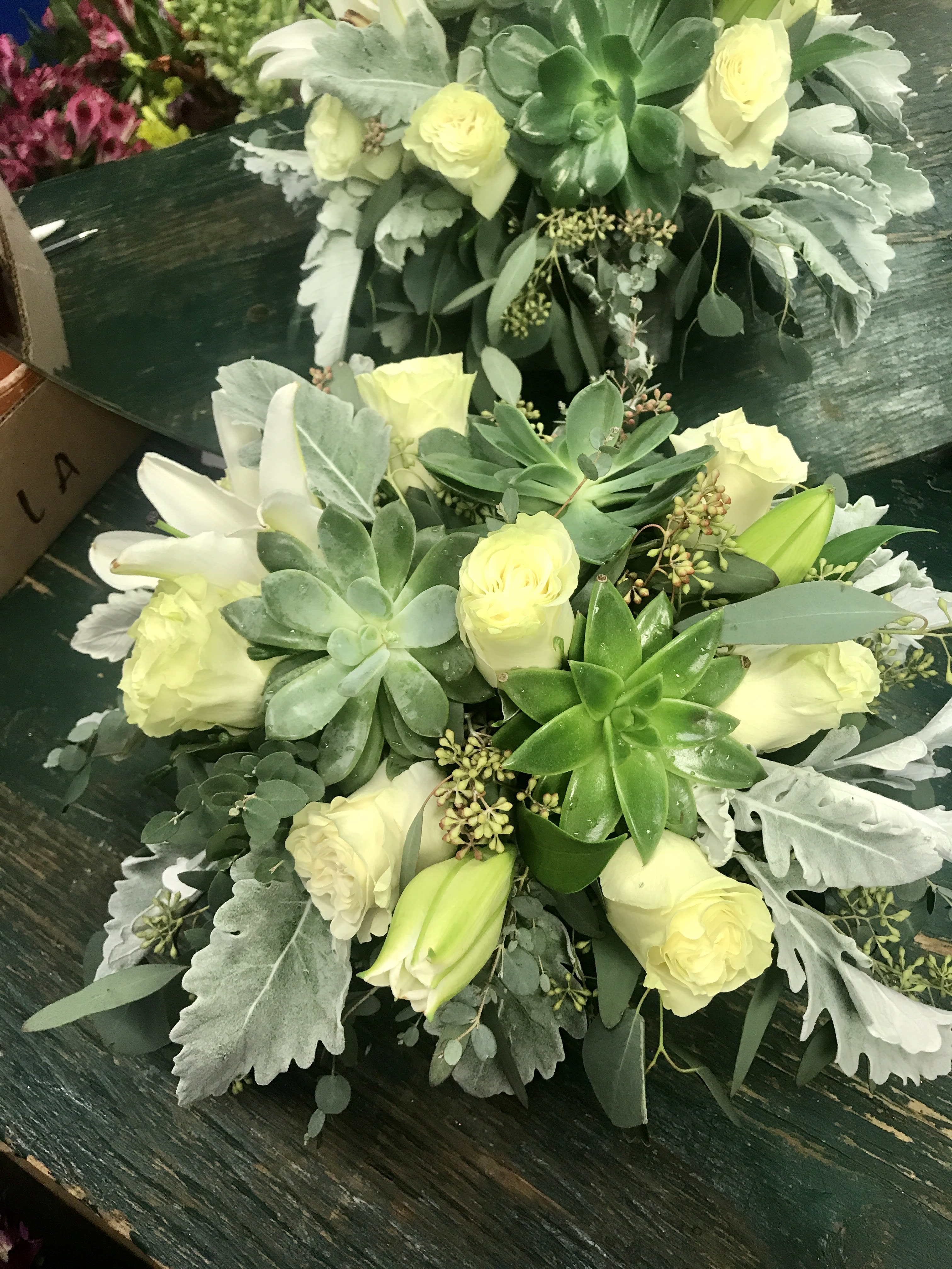 Two pale yellow rose and succulent bouquets on a dark table