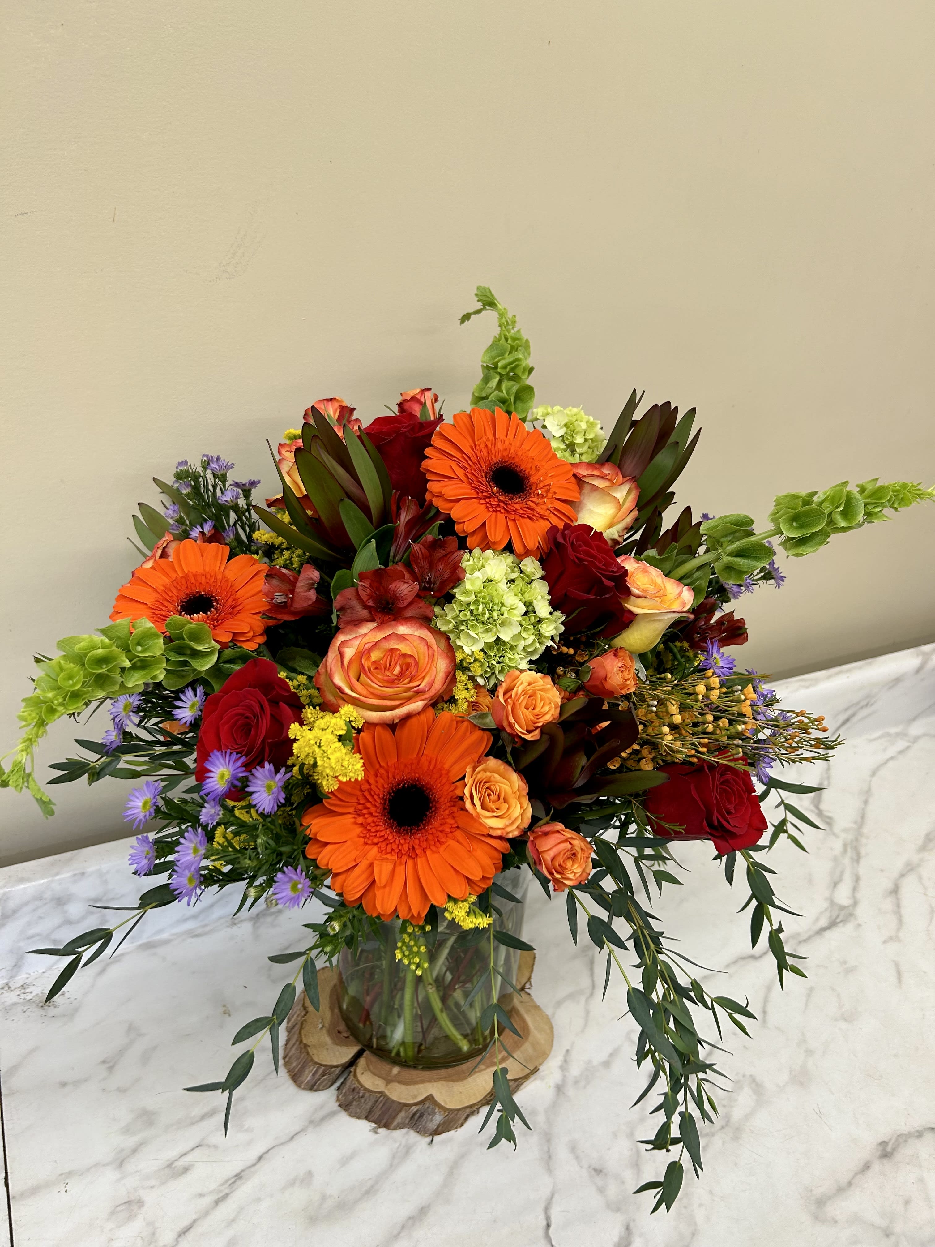 Bright mixed bouquet with orange gerbera daisies and red roses in a glass vase