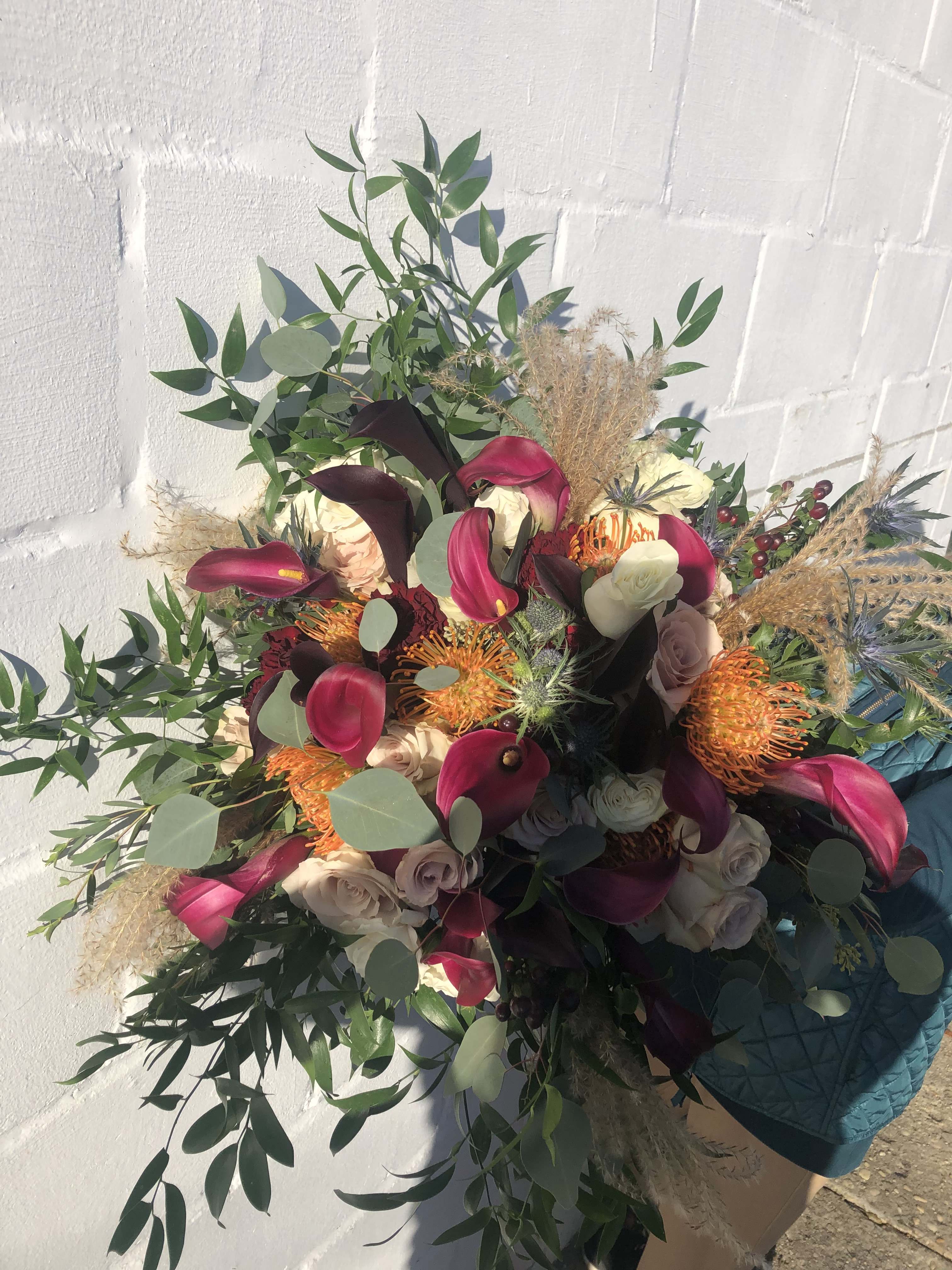 Large bouquet of burgundy calla lilies, cream roses, and orange protea with cascading greenery
