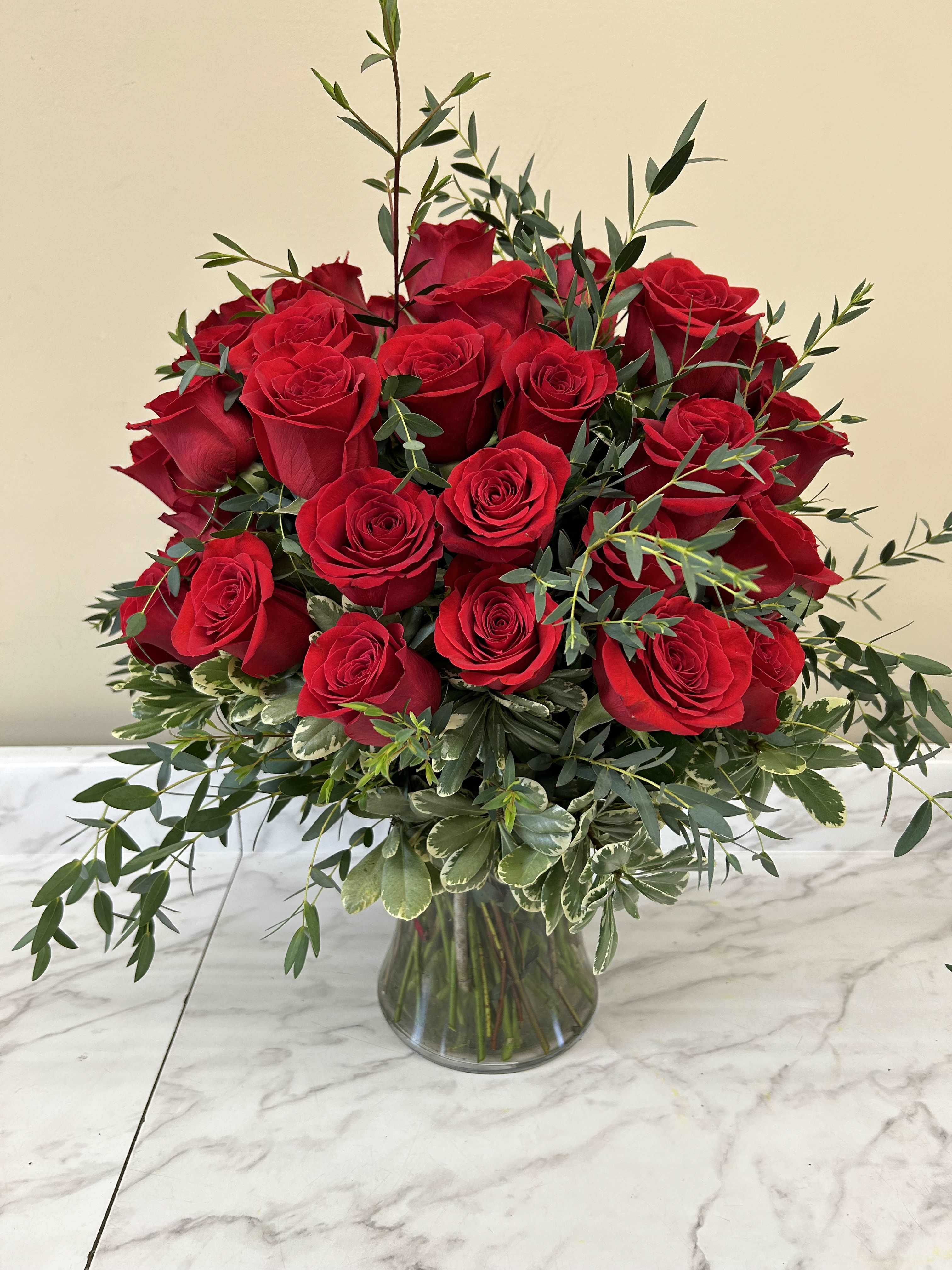 Red roses arranged in a clear glass vase with mixed greenery