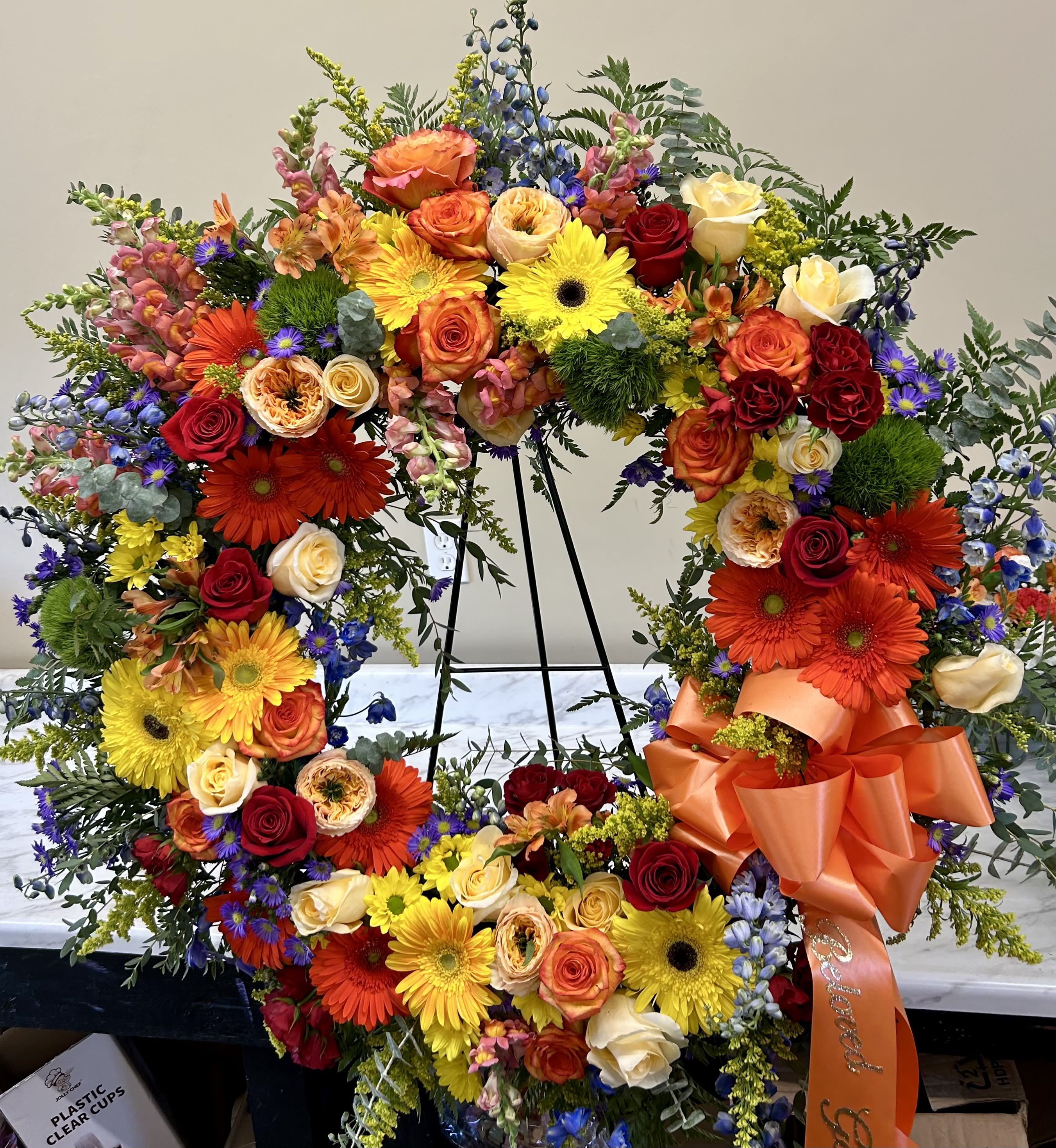 Large floral wreath with roses, gerbera daisies, and mixed blooms on a stand