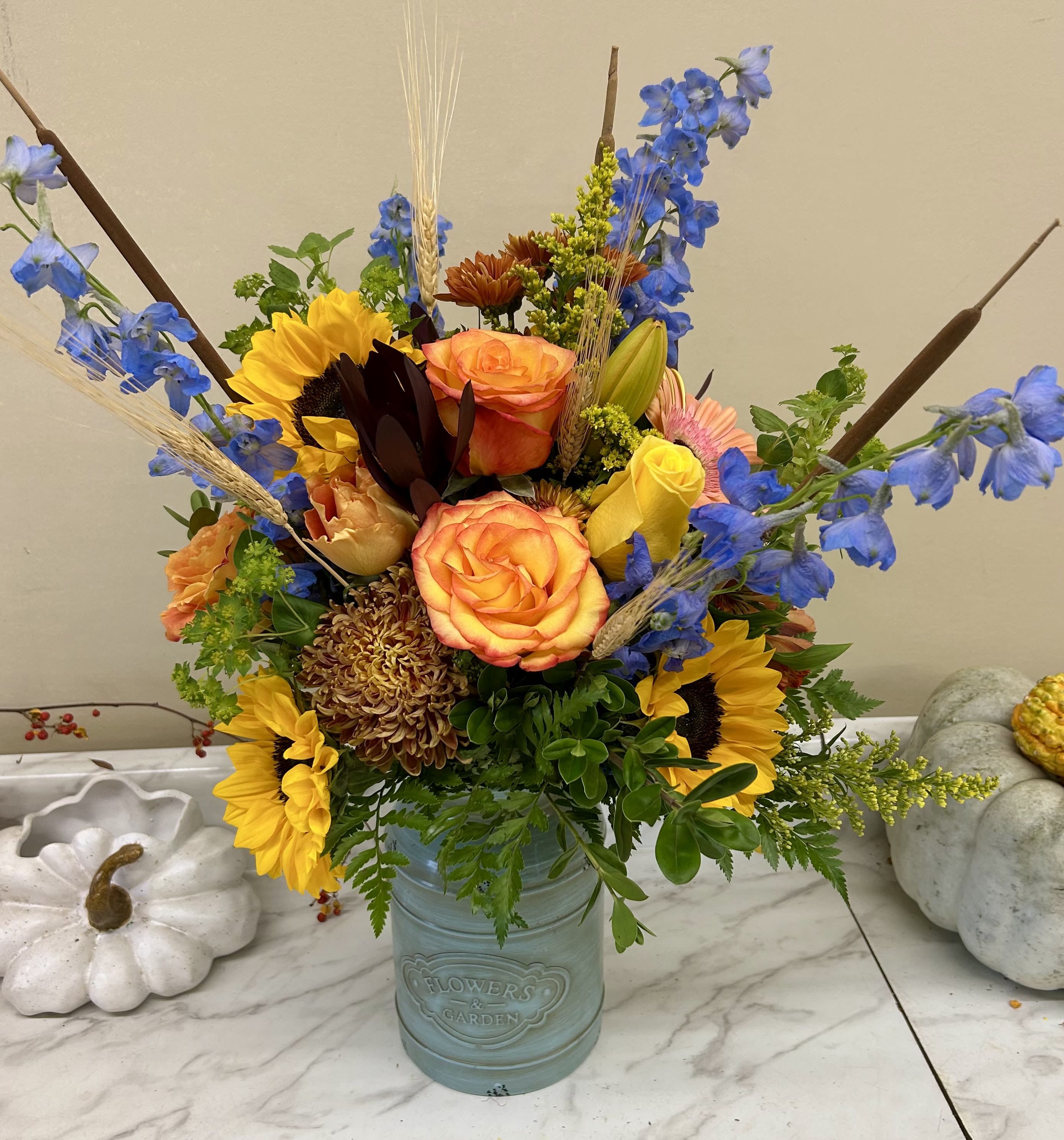 Mixed bouquet in a blue vase with sunflowers, roses, and blue delphinium