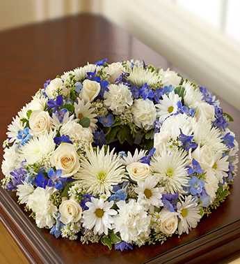 Cremation Wreath - Blue and White - Product ID: 95411  A beautiful remembrance, our blue and white table wreath arrangement is perfect for the cremation service or a memorial in the home. Elegant roses, delphinium, spider mums, carnations and daisy poms are crafted into a lovely wreath that pairs with a photo or urn to create a memorable tribute. Comforting table wreath arrangement of blue and white blooms such as roses, delphinium, spider mums, carnations, daisy poms and monte casino, gathered with variegated pittosporum and seeded eucalyptus Hand-crafted by our select florists to be sent to the cremation service to honor friends or family members Also appropriate for smaller memorial services in the home The cremation urn or a framed photograph can be placed in the center to present a lovely tribute at the service or home Large arrangement measures approximately 22"H x 22"L Small arrangement measures approximately 17"H x 17"L Our florists hand-design each arrangement, so colors and varieties may vary due to local availability
