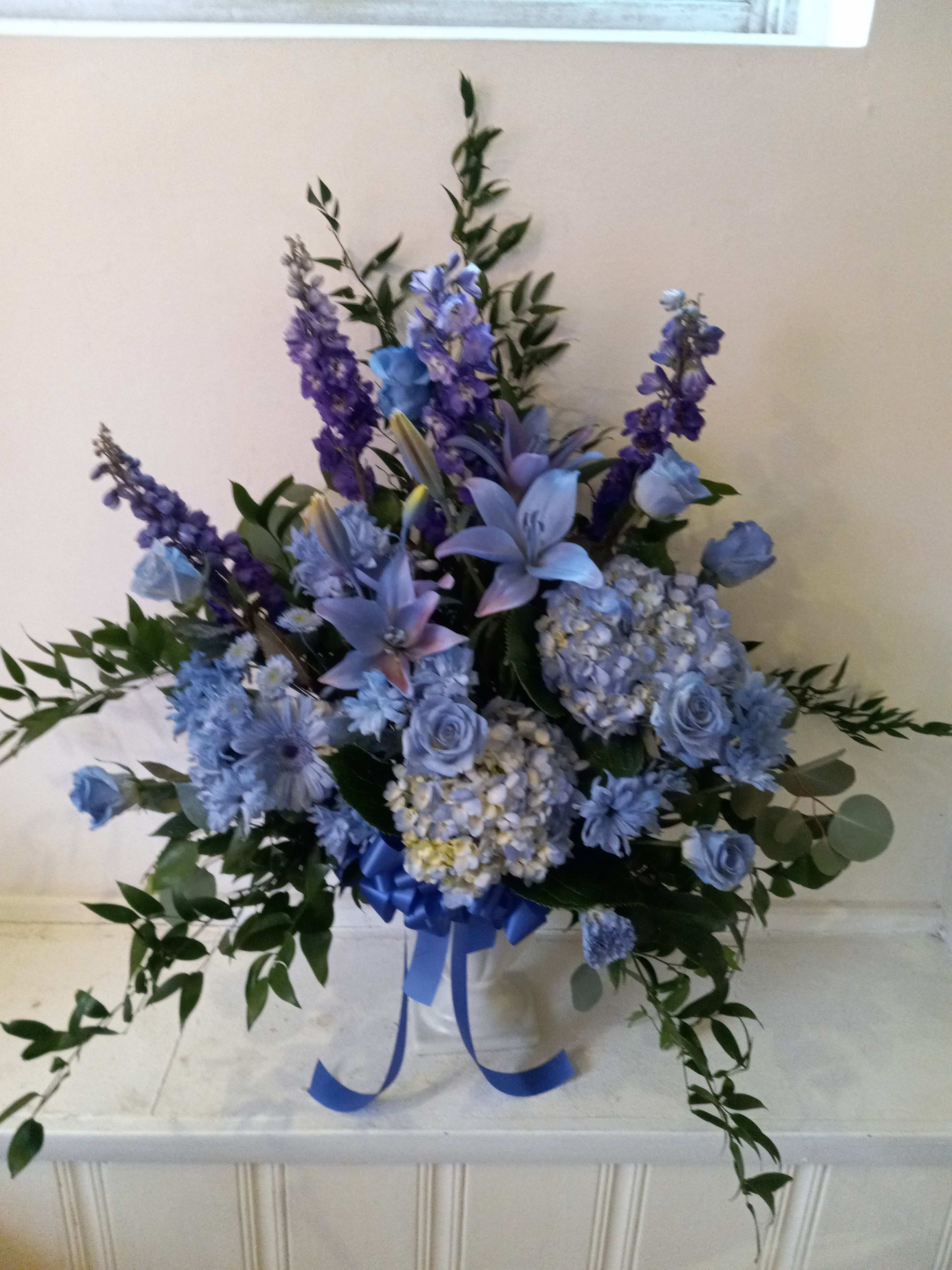 Blue and purple floral arrangement in a white container with a ribbon