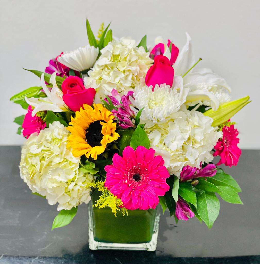 Bright mixed bouquet in a square glass vase with pink, white, and yellow flowers.