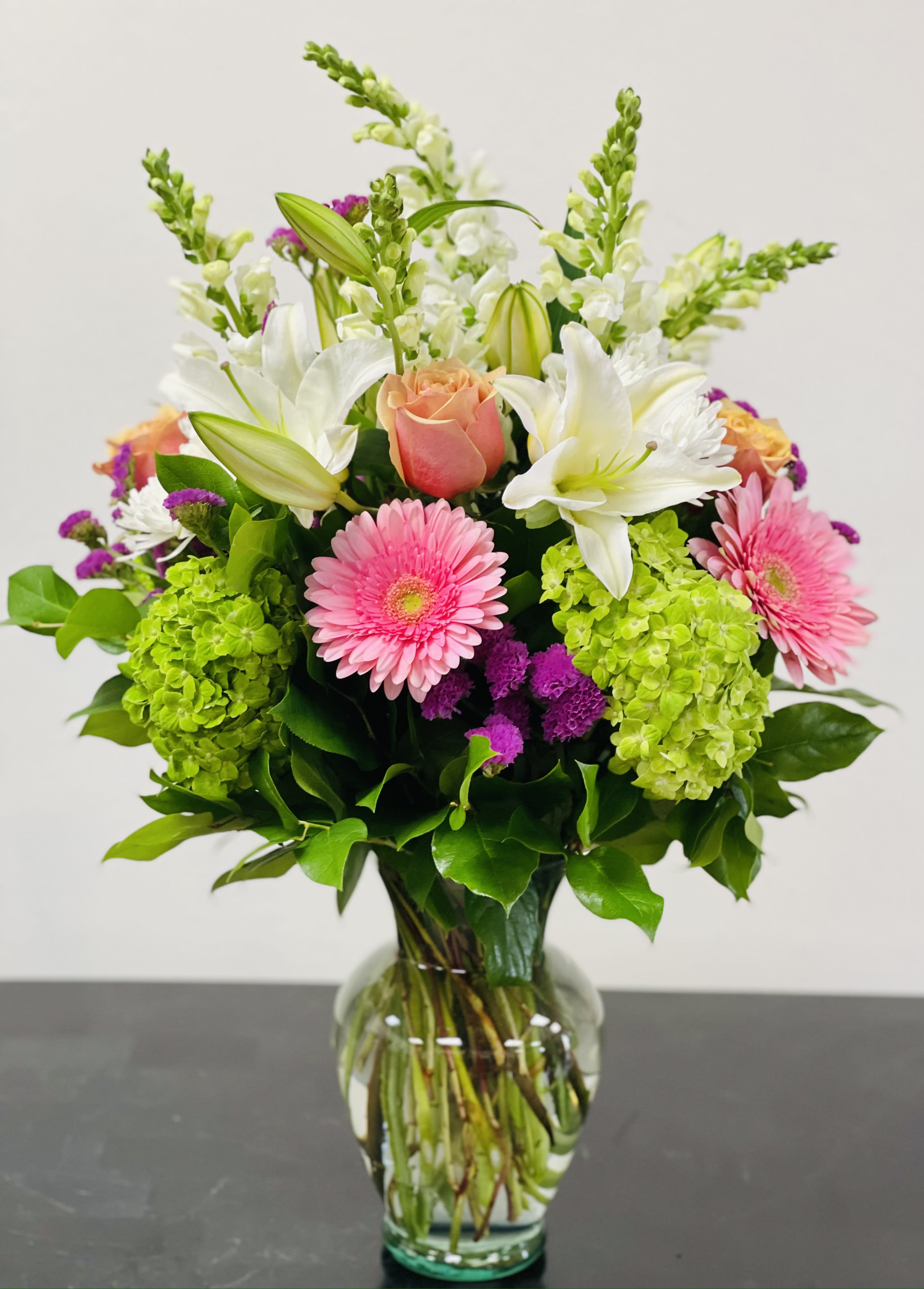 Mixed bouquet with pink gerbera daisies, white lilies, and green hydrangeas in a glass vase