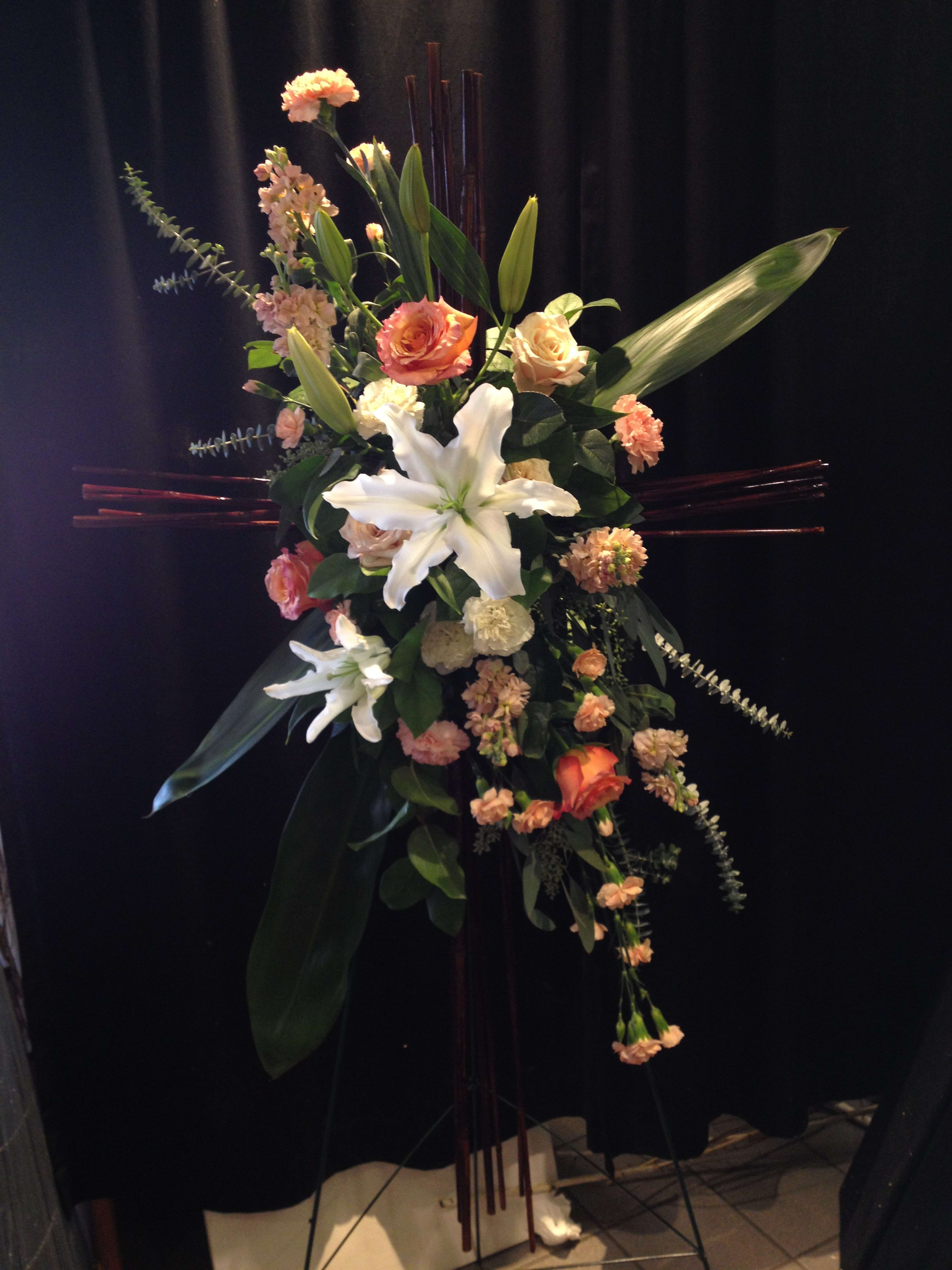 Standing floral spray with white lilies and peach roses on a dark easel