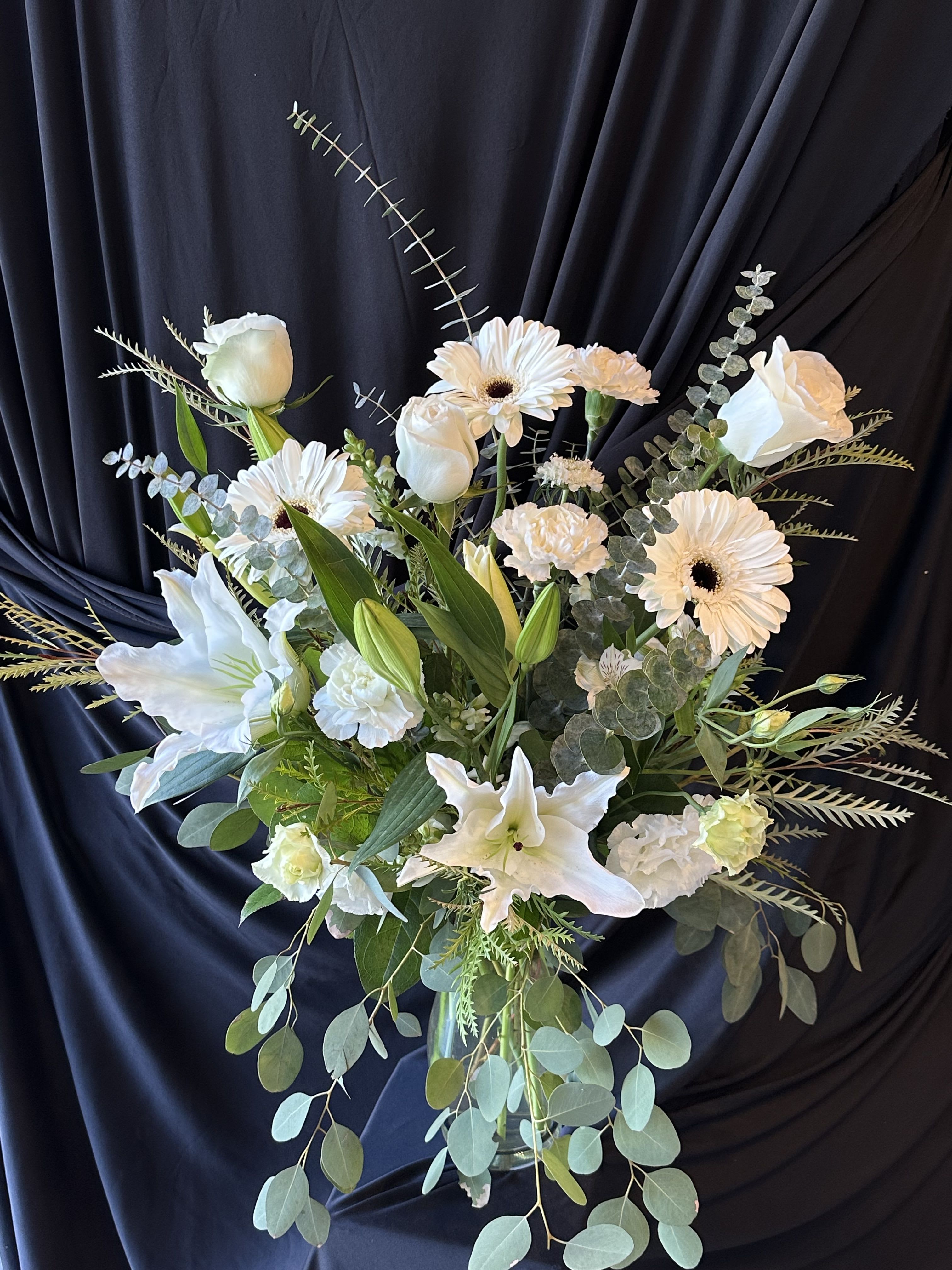White floral arrangement in a clear glass vase with lilies and daisies