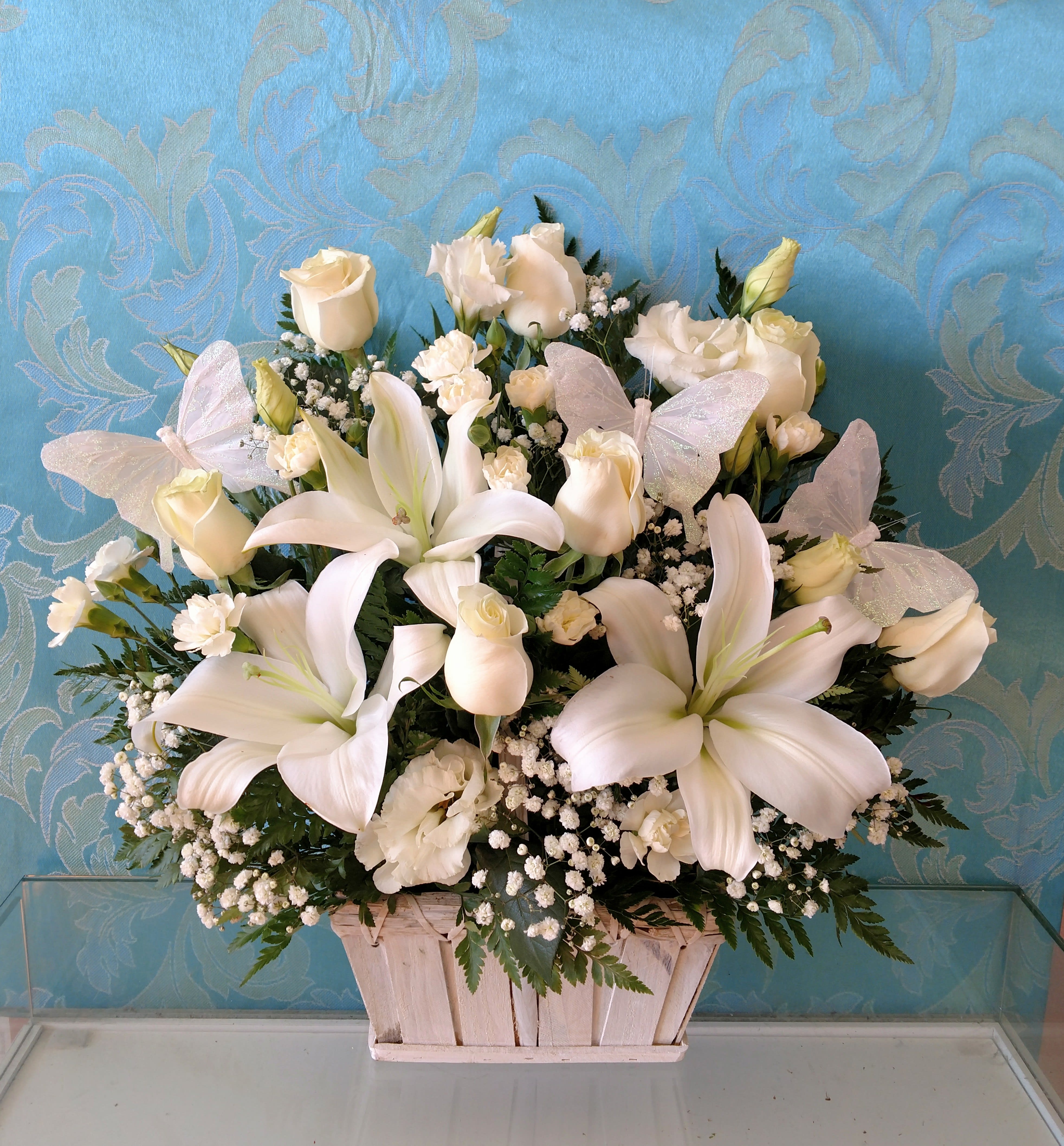White lilies and roses arranged in a wooden basket with butterfly accents