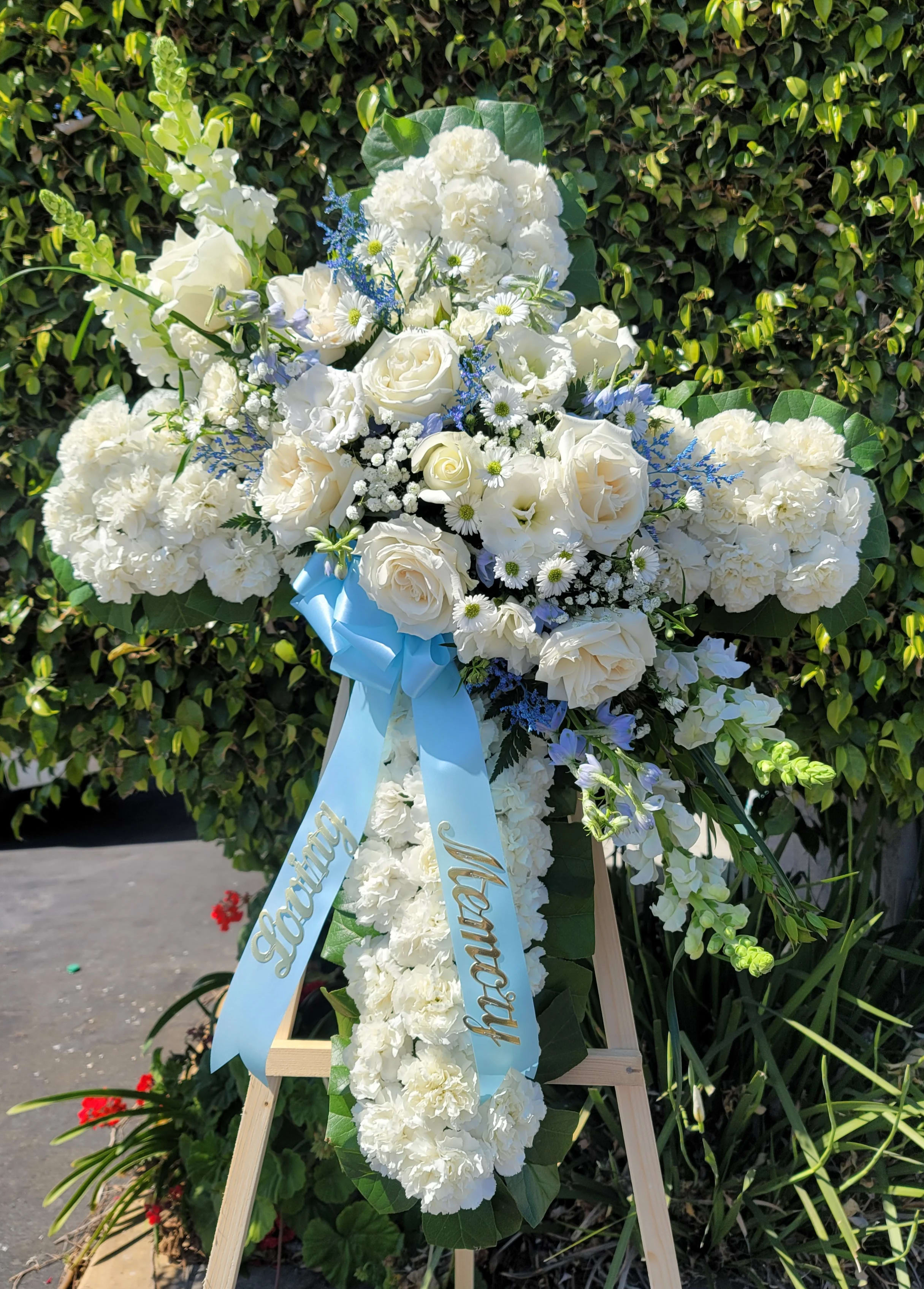 White floral standing cross on an easel with a blue ribbon