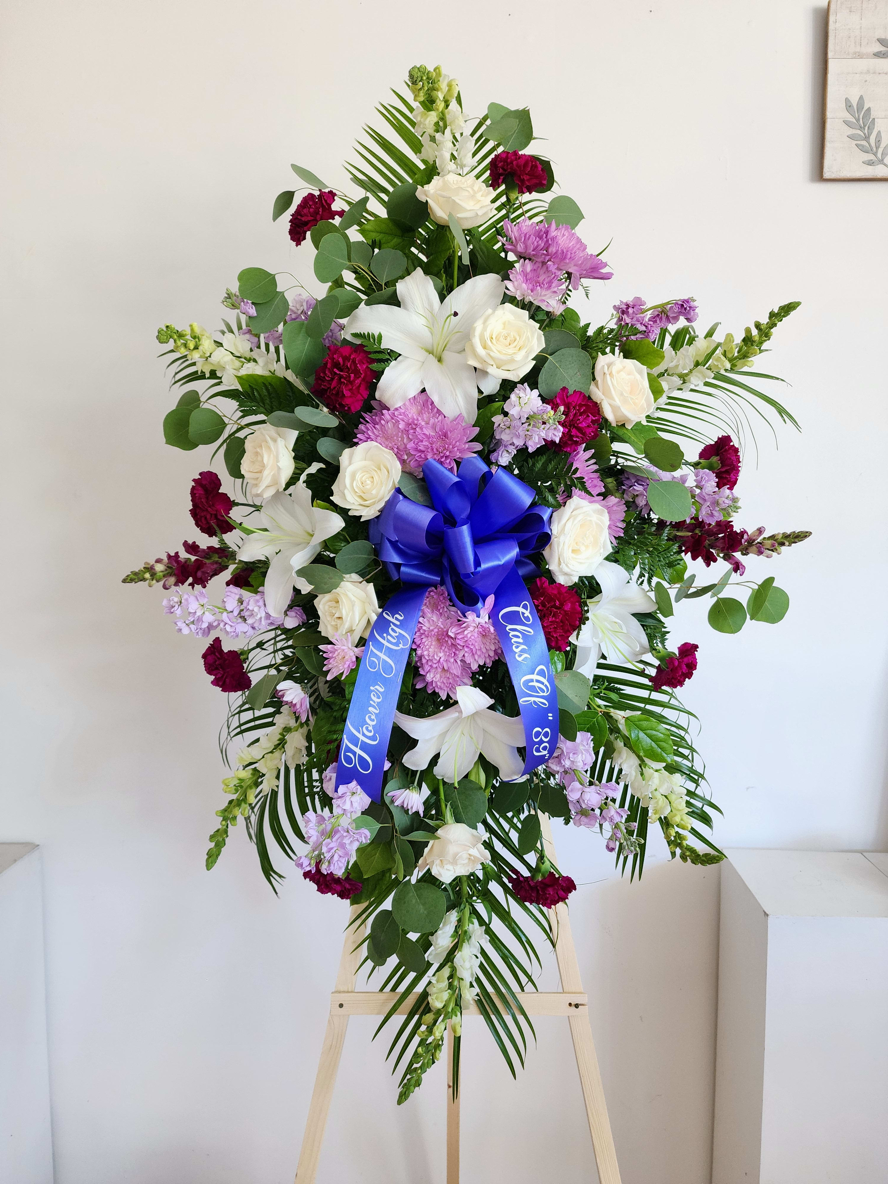 Tall funeral spray with white lilies, roses, and purple flowers on an easel