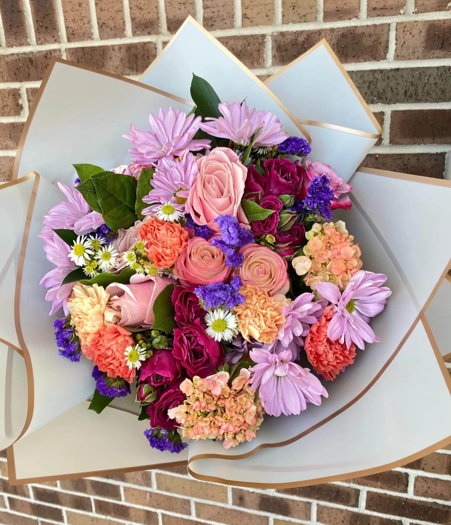 Mixed bouquet of pink, purple, and peach flowers wrapped in white paper