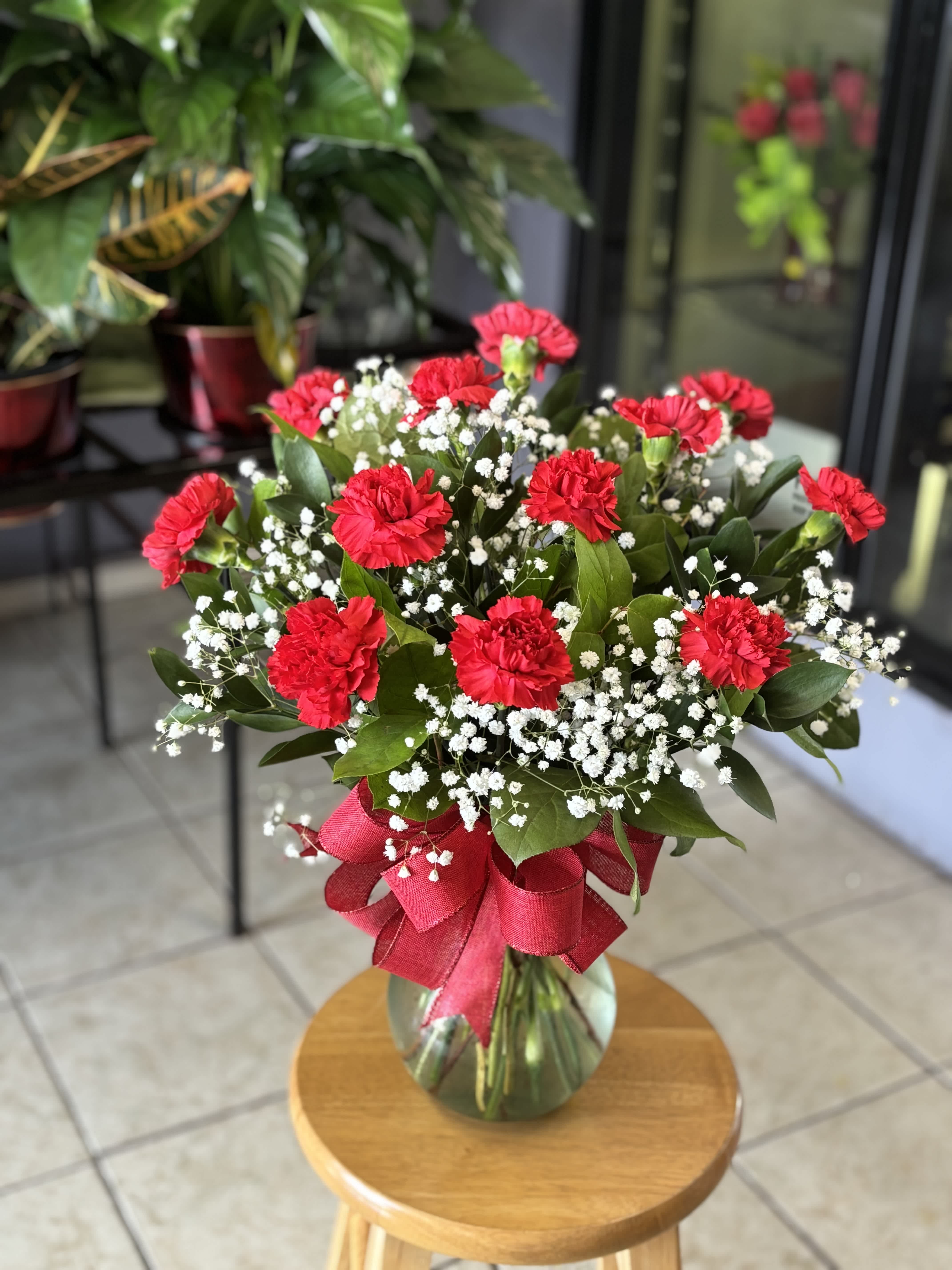 Red carnations and baby's breath in a glass vase with a red ribbon