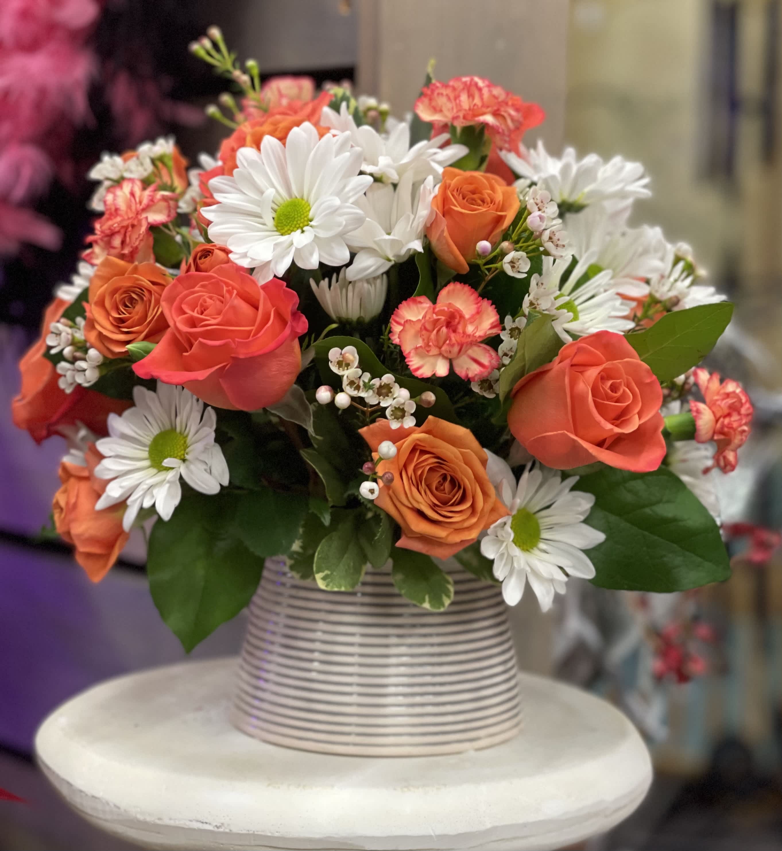 Bouquet of orange roses and white daisies in a striped vase