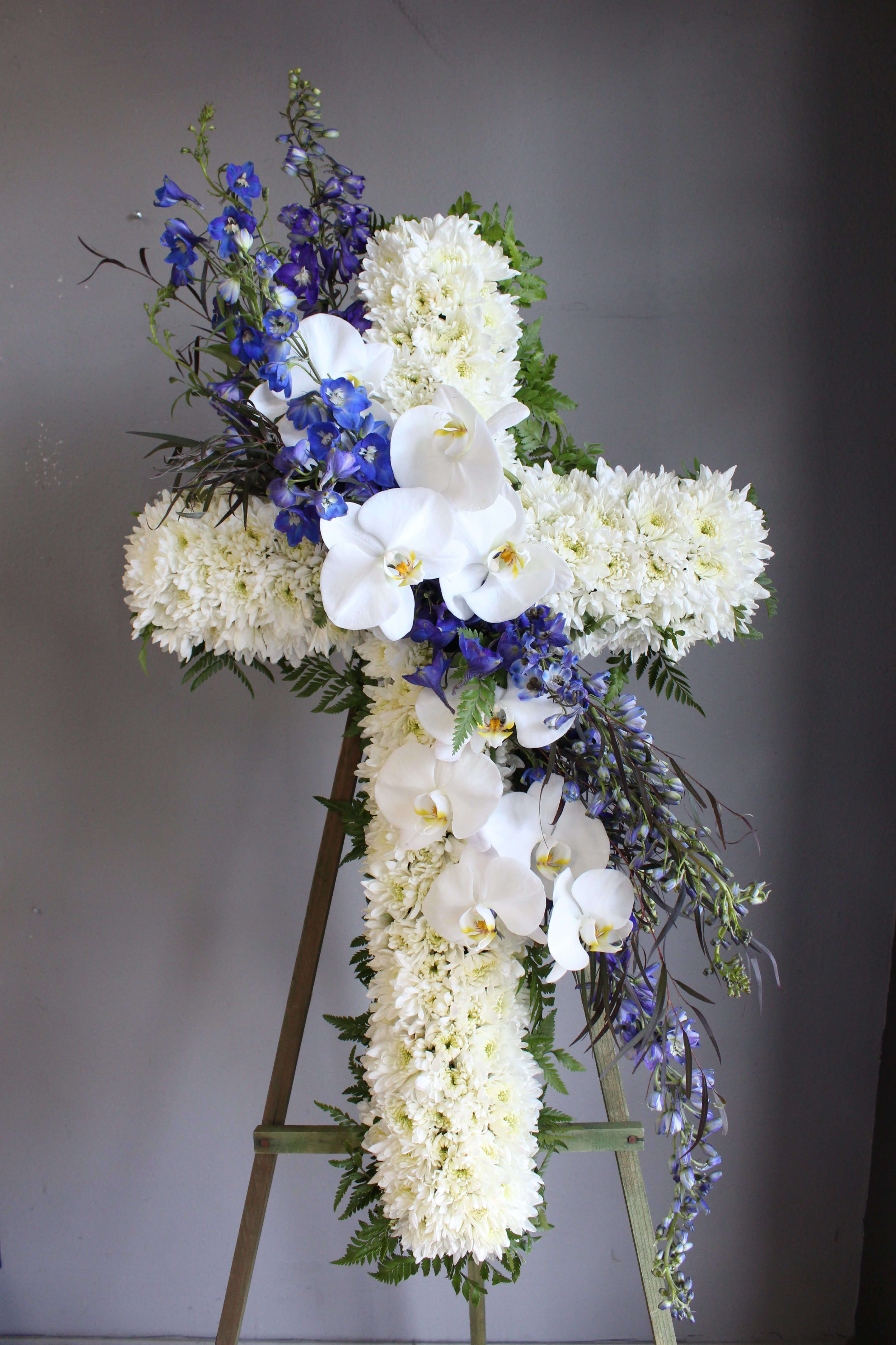 White floral cross arrangement with blue flowers on an easel