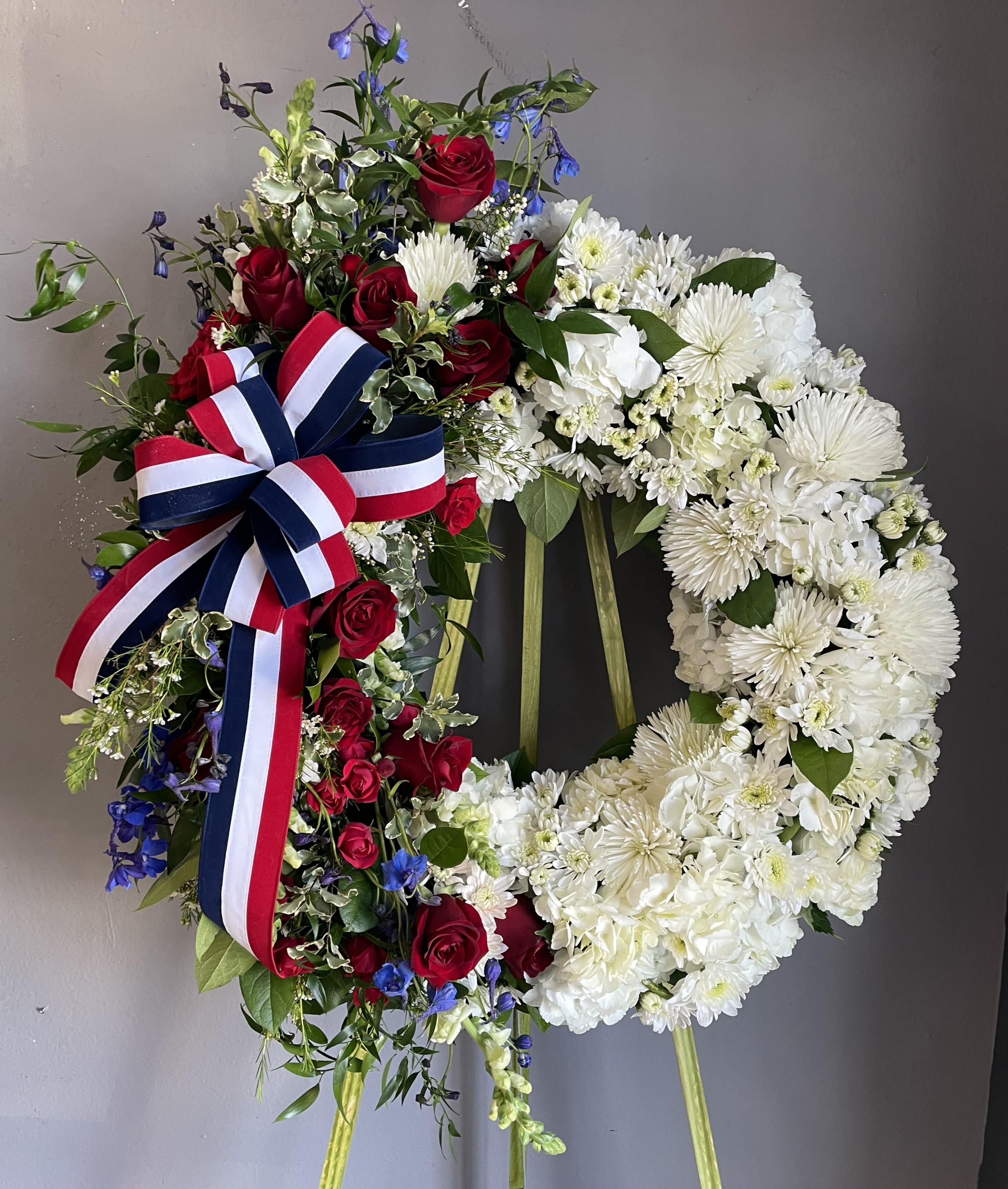 Two floral wreaths on stands, one red white and blue with roses and one white with chrysanthemums
