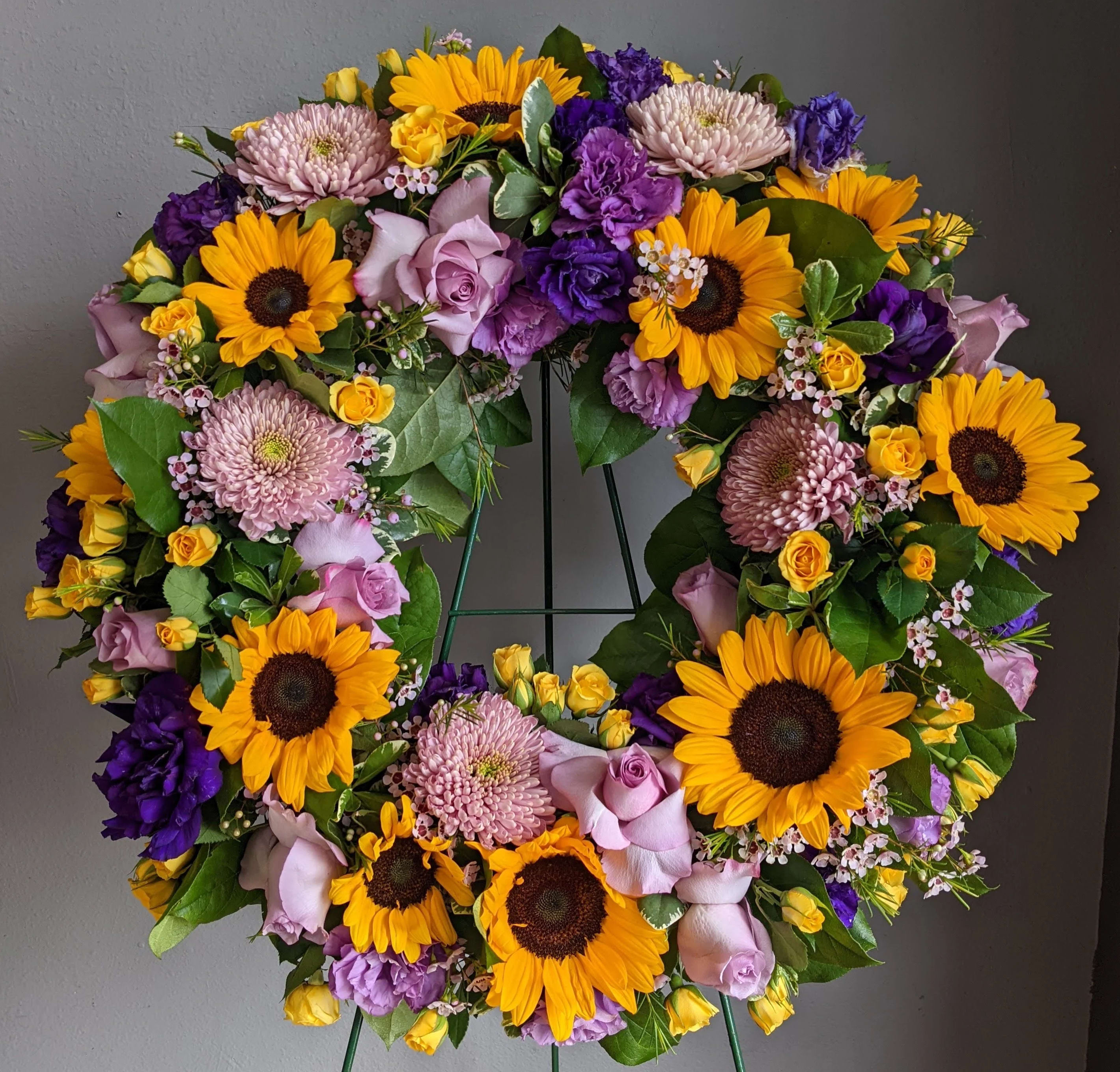 Circular wreath of sunflowers, roses, and purple blooms on a stand