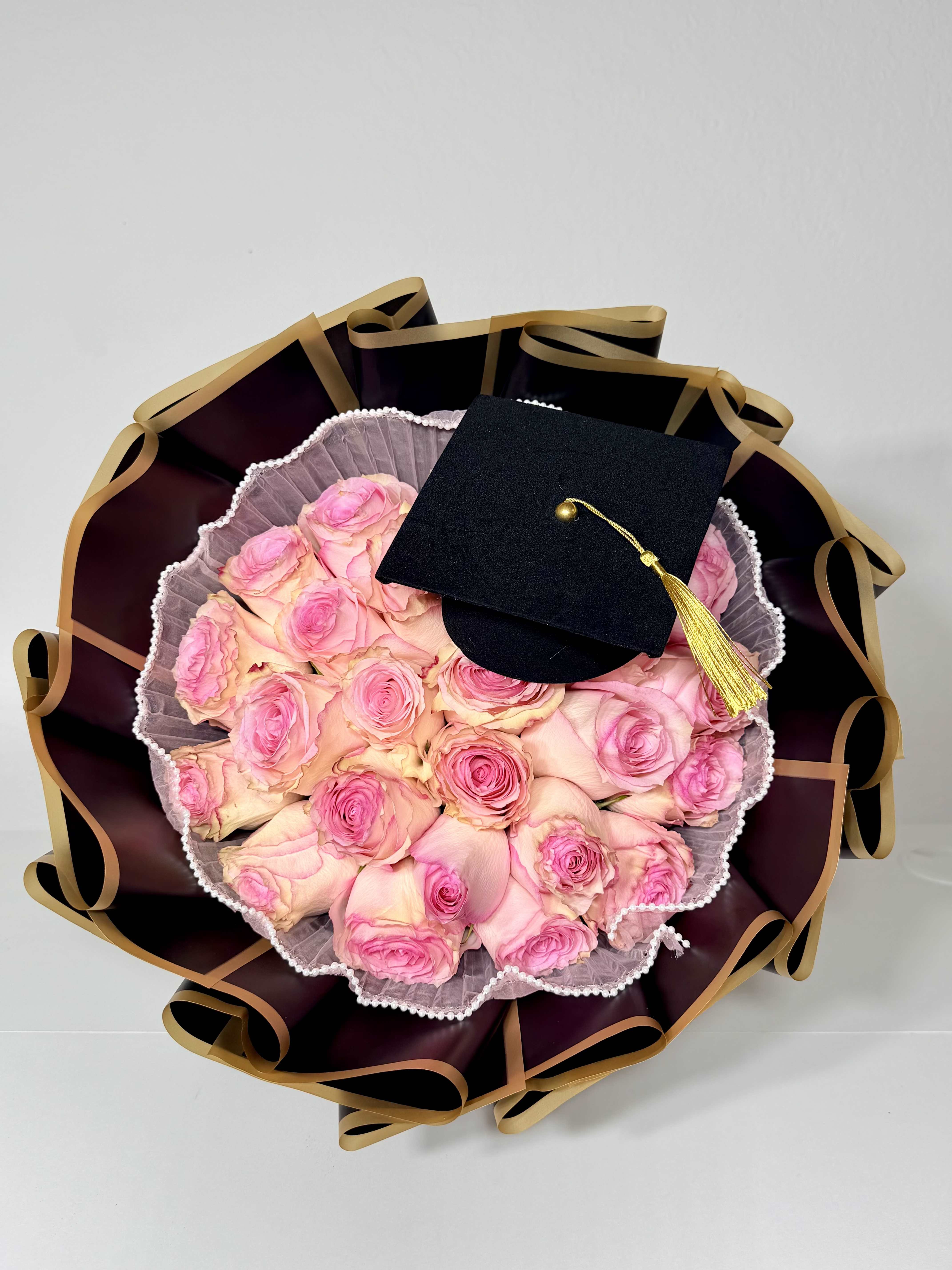 Graduation Bouquet - Celebrate their achievement with flowers as memorable as the moment. Designed with soft blush blooms, elegant black and gold wrapping, and a graduation cap detail, this bouquet was created to honor hard work, proud moments, and new beginnings