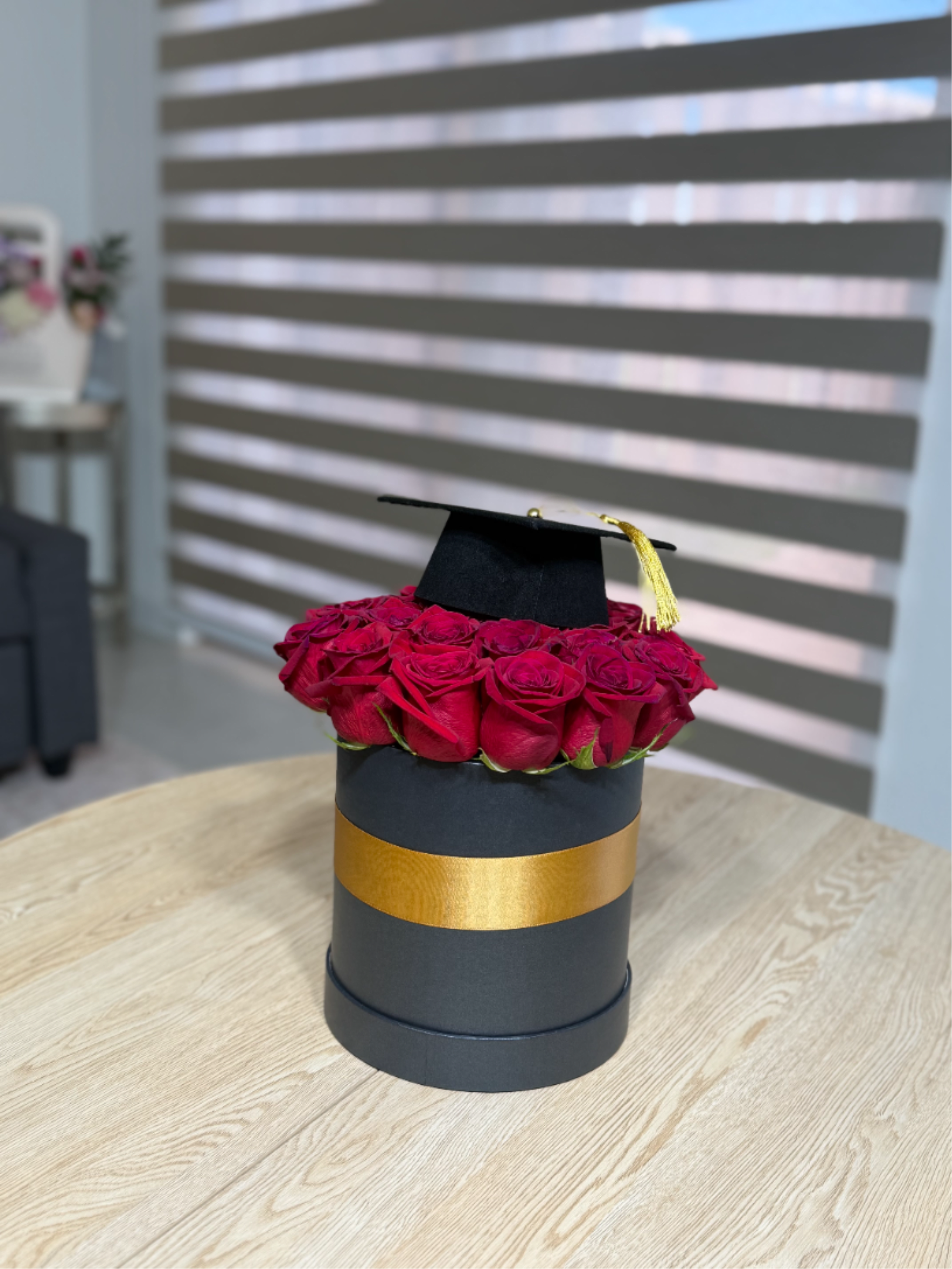 Red roses arranged in a black hat box with a graduation cap on top