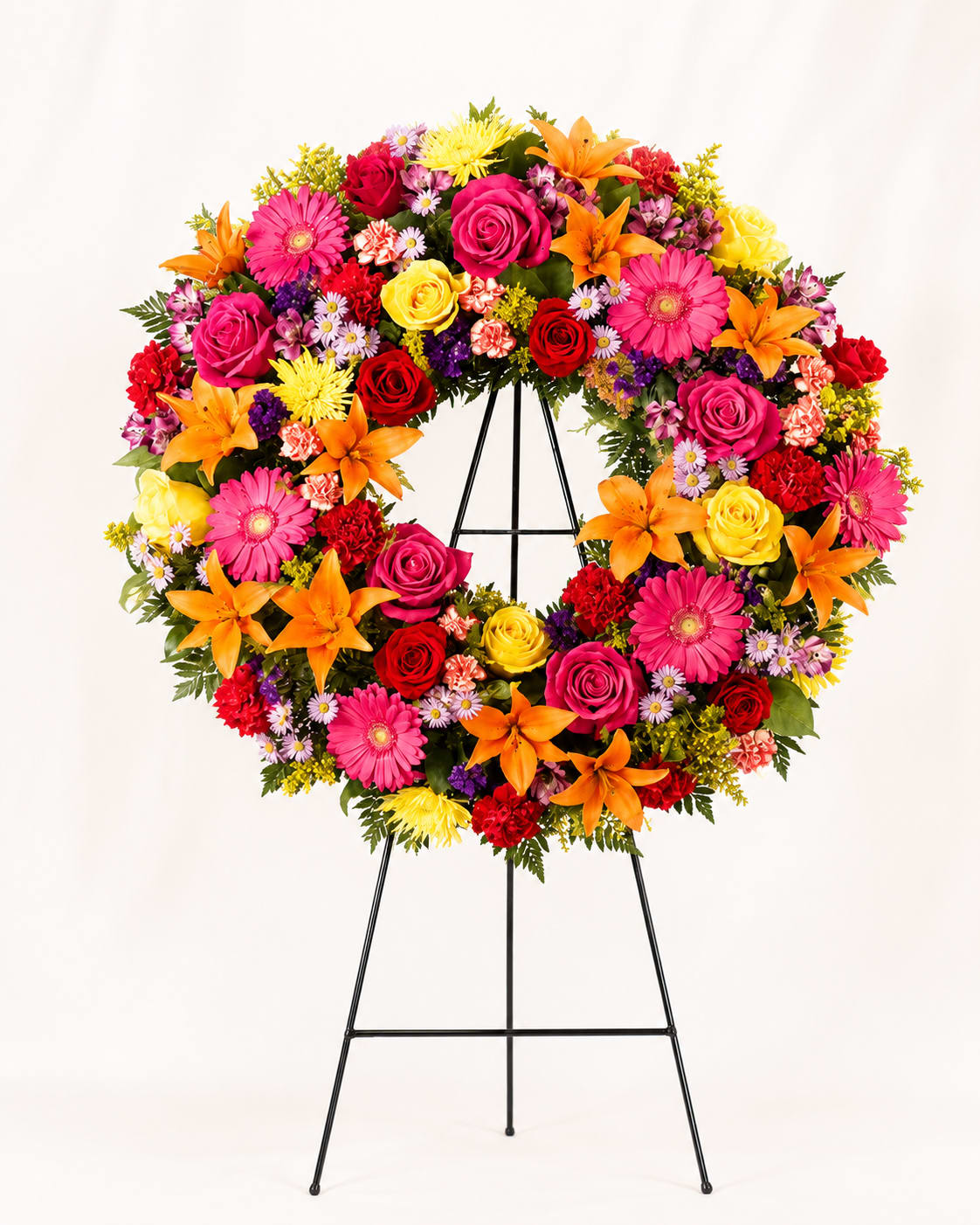 Memories Wreath - Bold, uplifting, and filled with color, the Bright Memories Wreath honors a life lived with joy and light. This radiant design blends roses, lilies, gerbera daisies, and seasonal blooms in shades of orange, fuchsia, yellow, and red- creating warm, celebratory expression of love.  This circular shape symbolizes eternity and the unending bond shared with those we cherish. Each flower is placed with intention, forming a wreath that feels both vibrant and heartfelt- a tribute that celebrates personality, passion, and the beautiful moments remembered forever.  
