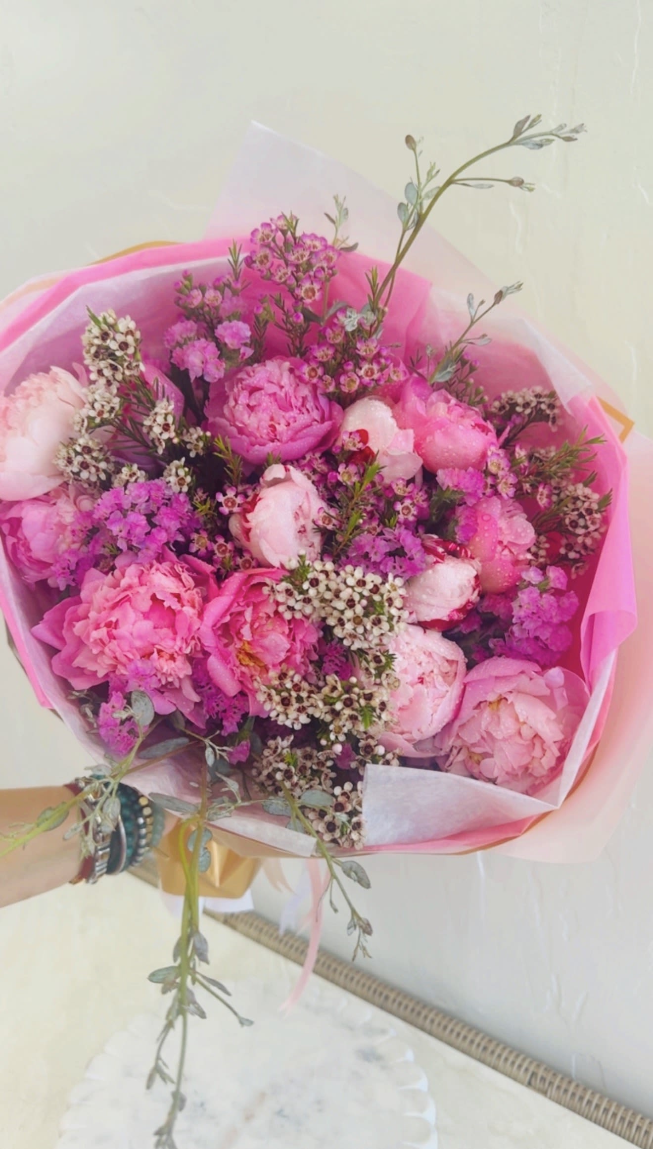 Whimsical Peonies Bouquet by The Flower Spot - Full, blushing pink peonies take center stage in this whimsical peonies bouquet, a romantic flower arrangement perfect for birthdays, spring celebrations, or a heartfelt romantic gesture. The design reads light and feminine-long, airy stems and a loose hand-tied silhouette give the person you're thinking of a fresh-picked, effortless charm that feels both joyful and intimate.  Clusters of small white and magenta filler blooms weave between the peonies, with touches of green foliage adding crisp contrast. The bouquet is wrapped in layered pink and white paper and finished with a ribbon, creating a soft, elegant presentation that looks lovely on arrival and on display. Sized as a generous hand-tied bouquet, it arrives ready to place in a vase; trim stems and refresh water to extend the life of the blooms. Each flower has been carefully curated and arranged by our designer to make the recipient feel truly celebrated.