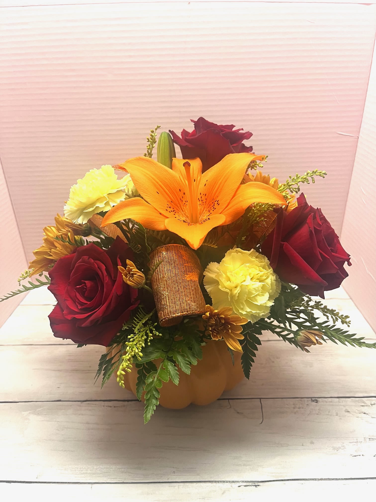 Bouquet of red roses, orange lily, and yellow carnations in a pumpkin container