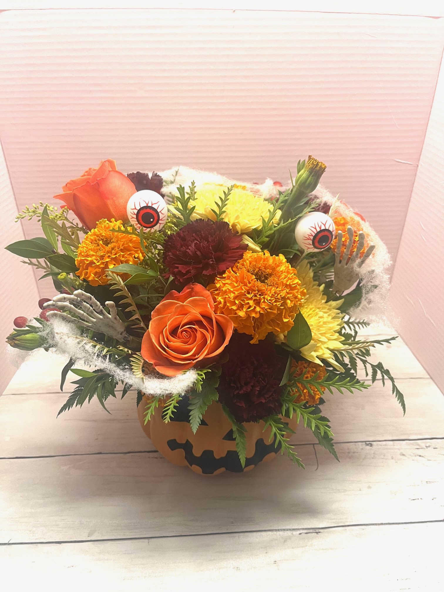 Halloween bouquet in a pumpkin container with roses, marigolds, and eyeball picks