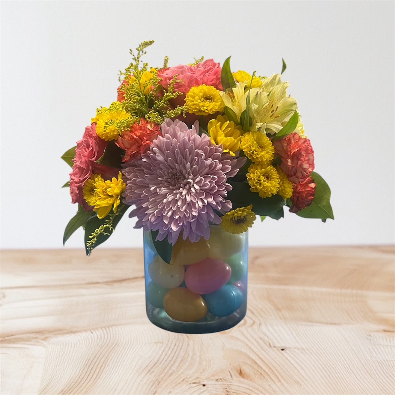 Colorful mixed flower arrangement in a blue glass vase filled with pastel eggs