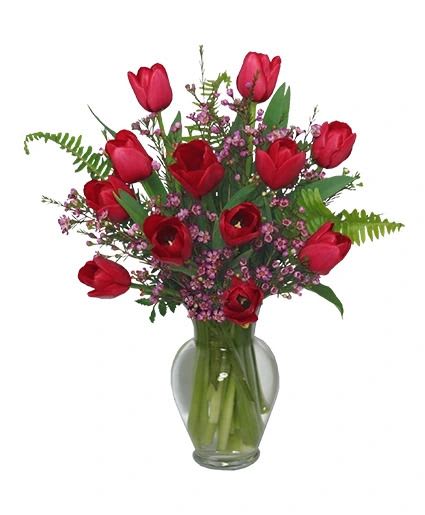 Red tulips and small pink flowers arranged in a clear glass vase