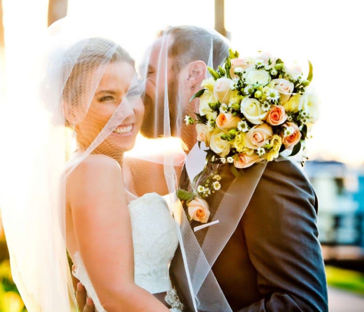 Bride and groom under a veil, holding a bouquet of pale roses