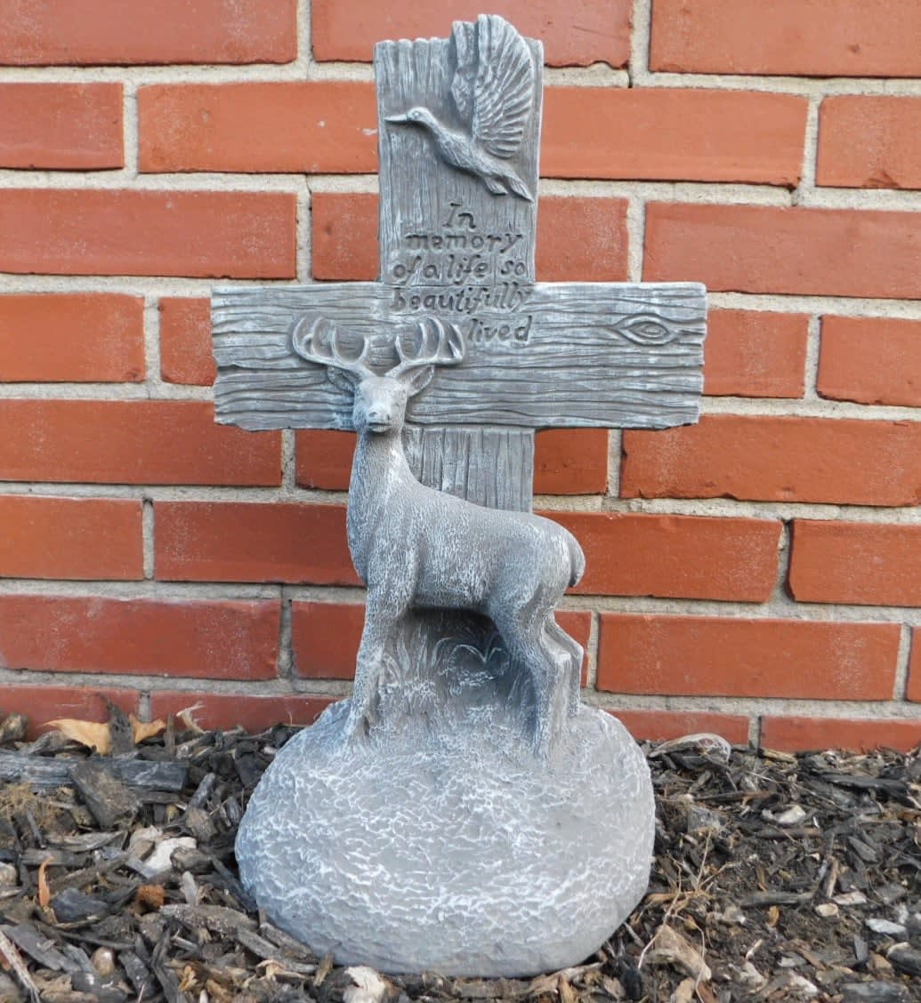 Gray memorial cross with a deer and bird relief against a brick wall