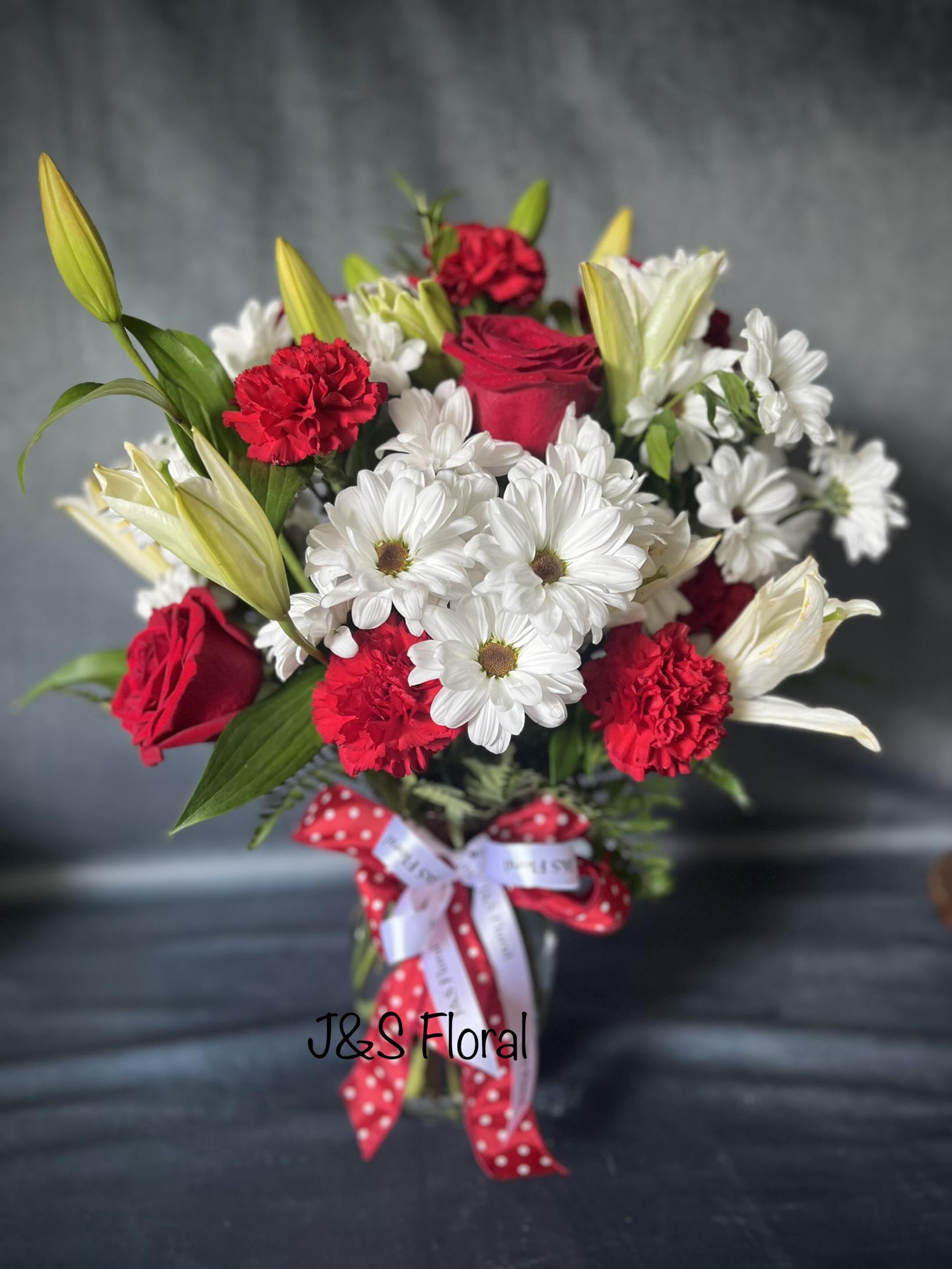 Bouquet of red roses, white daisies, and red carnations in a glass vase
