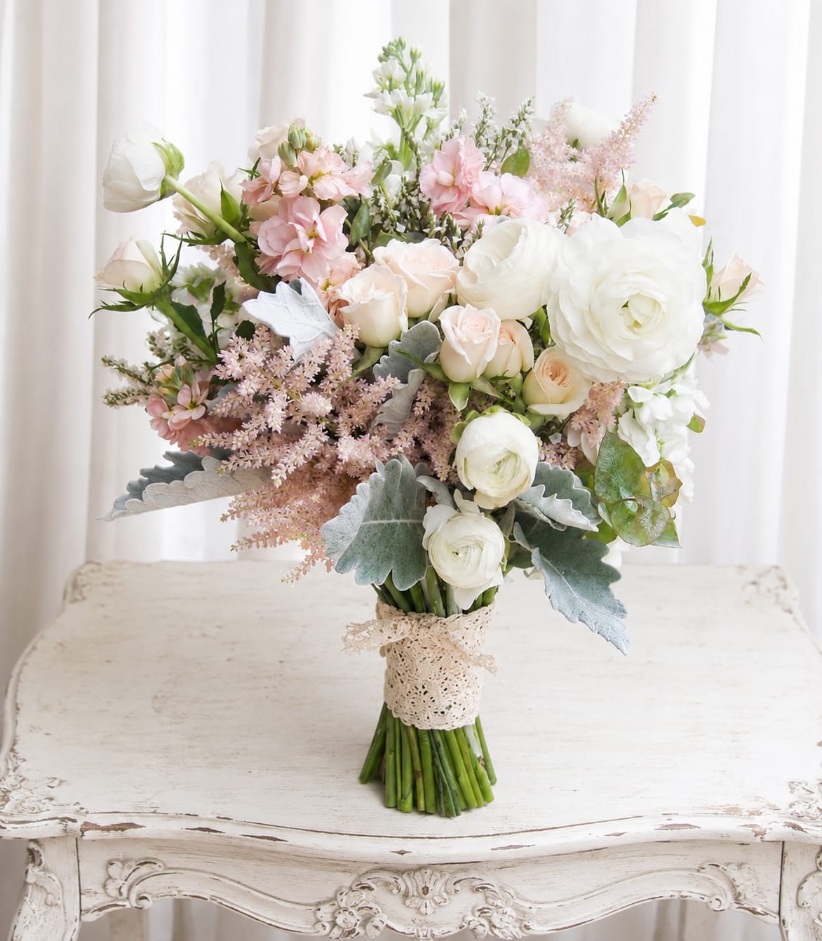 Beautiful wedding bouquet - Soft white blooms paired with blush pink roses and peachy ranunculus create a romantic wedding bouquet that feels both timeless and freshly garden-picked - ideal for a bride, bridesmaid, or a special anniversary gift. The arrangement reads as a wedding bouquet and will make the person you're thinking of feel cherished and luminous on their big day or during a milestone celebration.  The mix includes large white flowers, blush pink roses, ranunculus, stock, and airy pink filler blooms set against pale green-gray foliage for a textured, garden-style look. Stems are gathered tightly and finished with a delicate lace ribbon, giving the bouquet a handcrafted, vintage-inspired touch. Its soft palette of white, pink, peach, and green photographs beautifully and complements both classic and rustic wedding styles.  Choose this bouquet for a bride who wants understated elegance or for an anniversary that calls for a sentimental, wearable bouquet. Care: keep stems in water until ready to wear and mist lightly to preserve freshness; order timing is recommended to ensure peak blooms for the event.   If any design elements are of major importance to your order, please include them in the florist instructions at checkout or contact us to ensure availability.