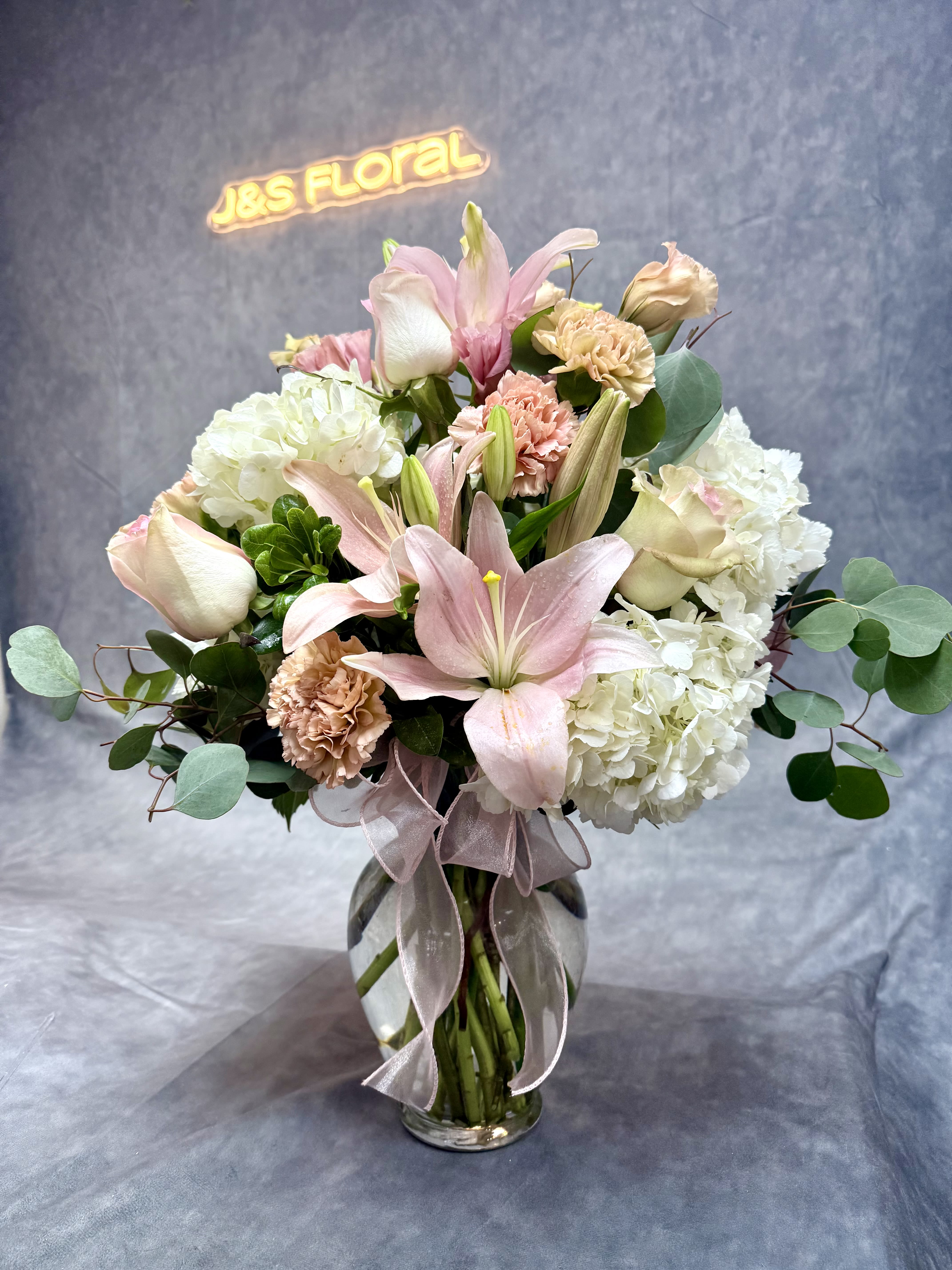 Pink lilies and white hydrangeas in a glass vase with a ribbon