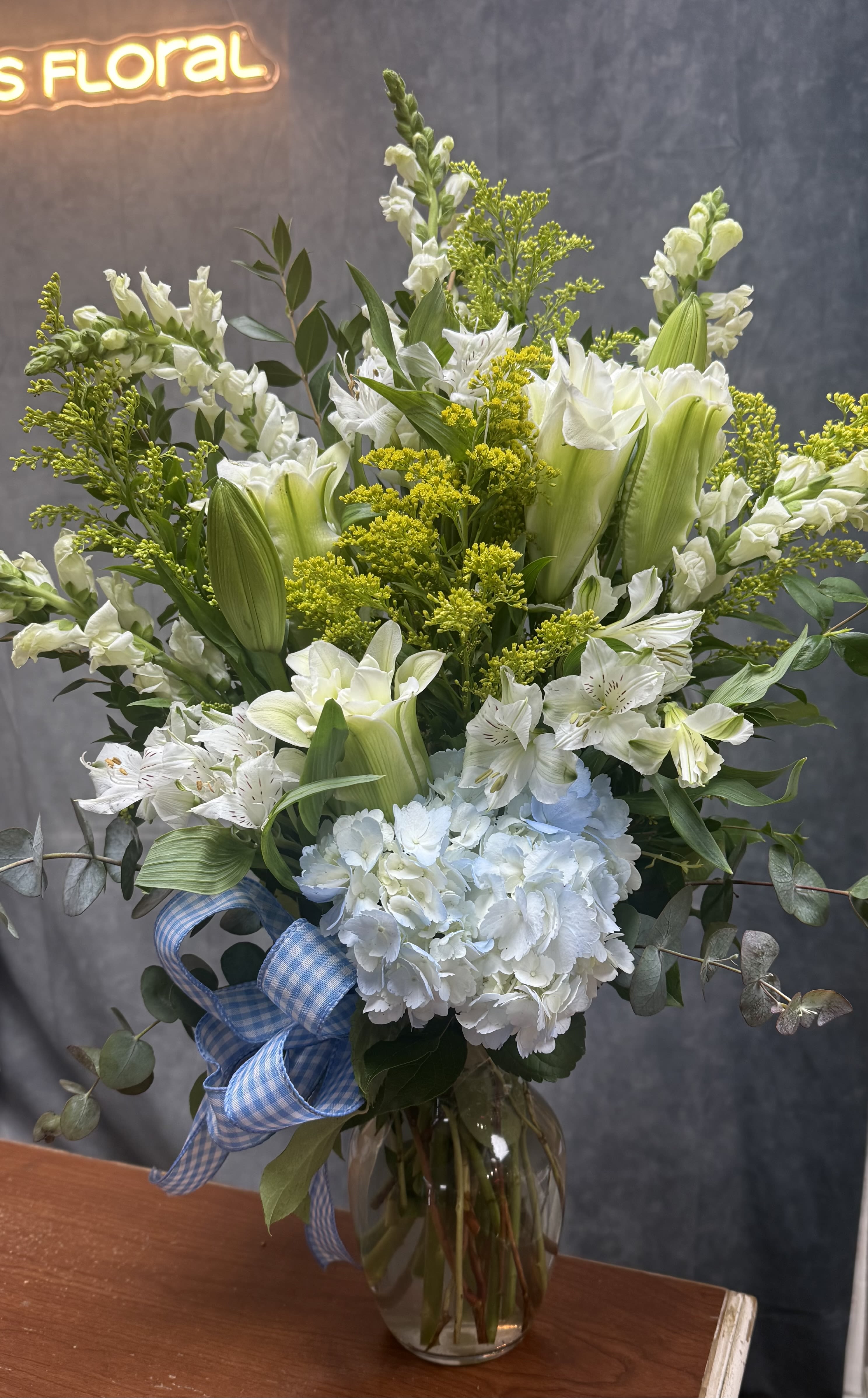 White and pale green floral arrangement in a glass vase with a blue ribbon