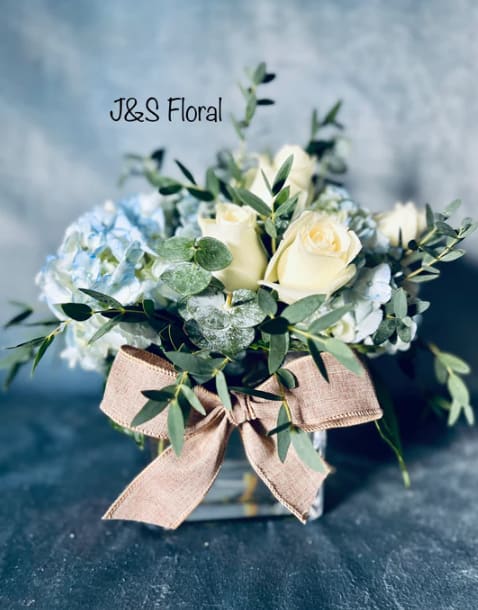 White roses and blue hydrangeas in a glass vase with a burlap bow