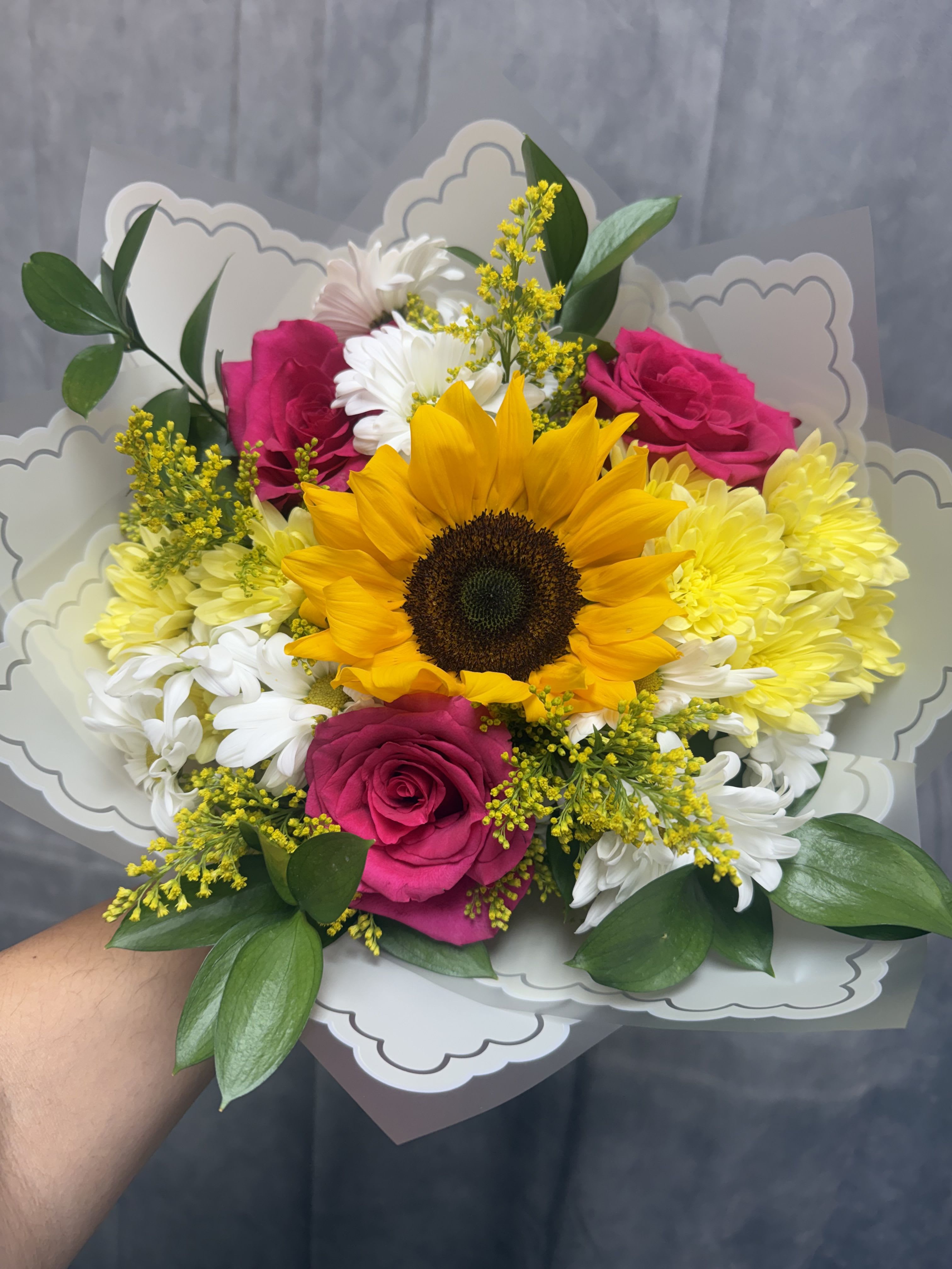 Bright Blooms Bouquet  - Bursting with cheerful color, this vibrant bouquet features a radiant sunflower, hot pink roses, bright cushions, golden solidago, and fresh greenery. Wrapped in elegant decorative paper, it’s the perfect arrangement to spread happiness, celebrate a special occasion, or brighten someone’s day with a touch of sunshine. 