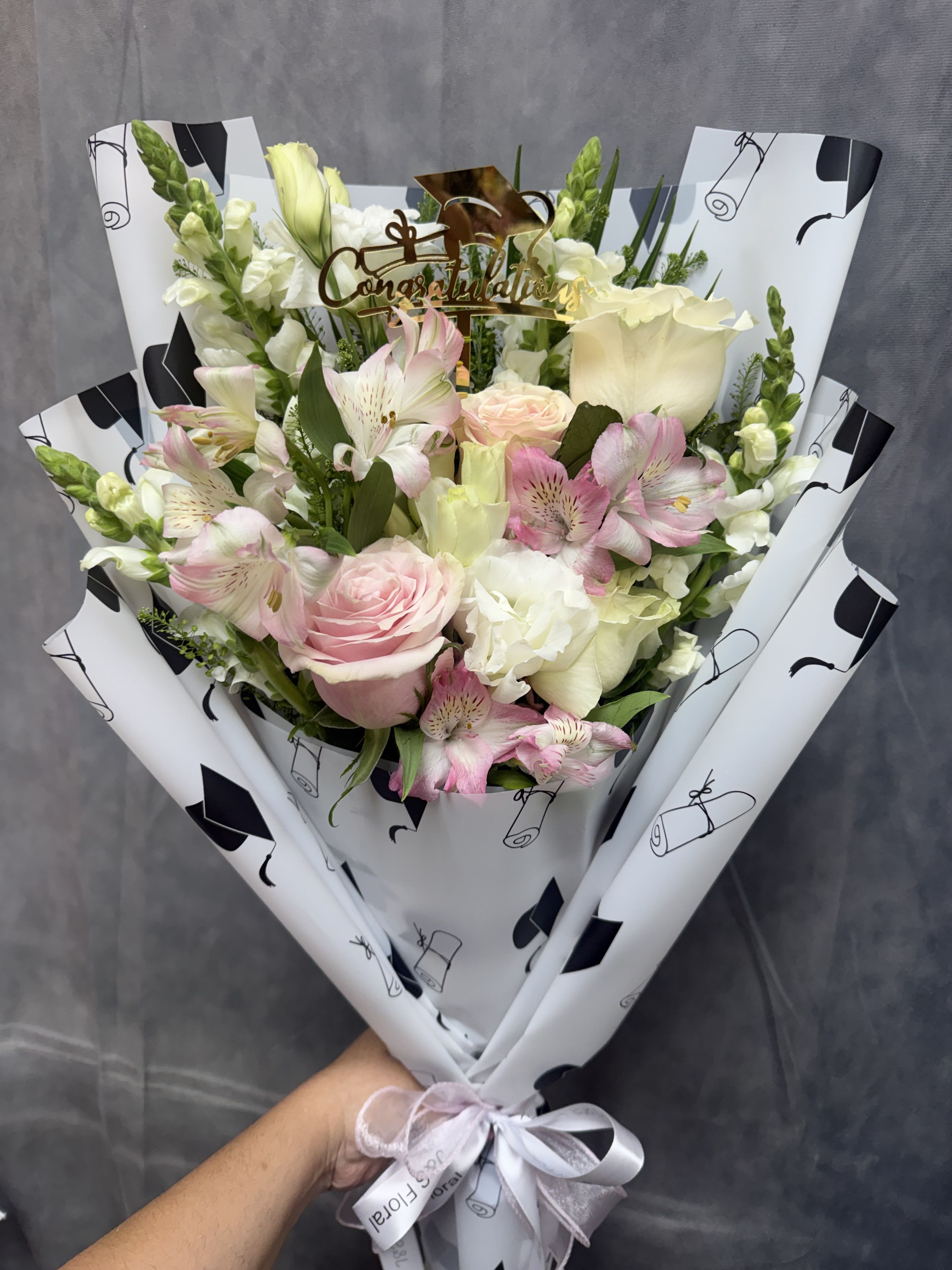 Blush celebration bouquet - White and pink roses, lisianthus , alstroemeria and snapdragons and greenery in elegant black-and-white wrap and a "congrats" topper-perfect for milestone celebrations.