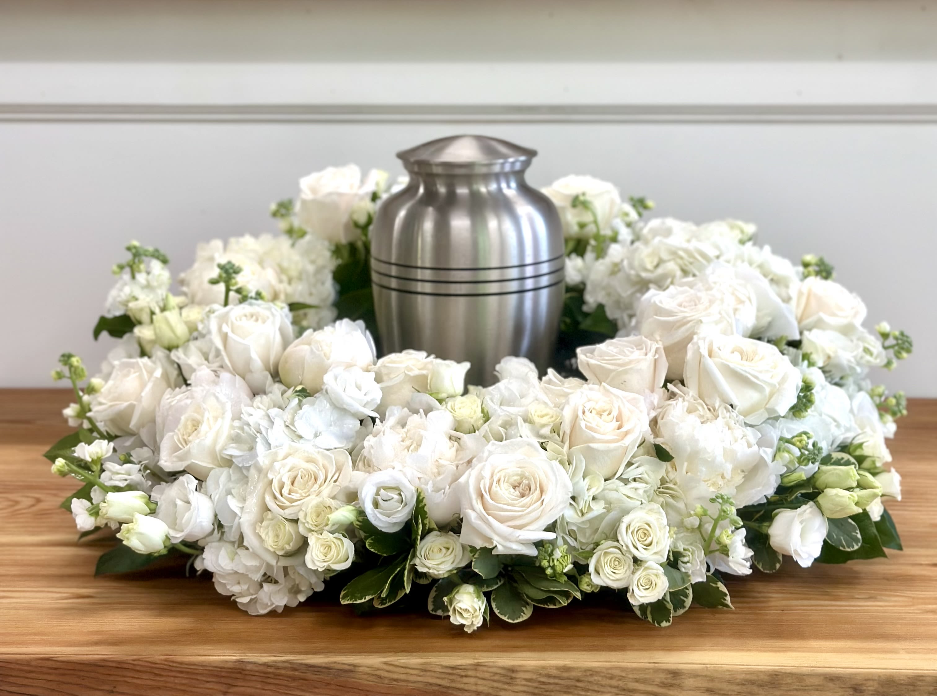 White rose and hydrangea funeral wreath around a silver urn