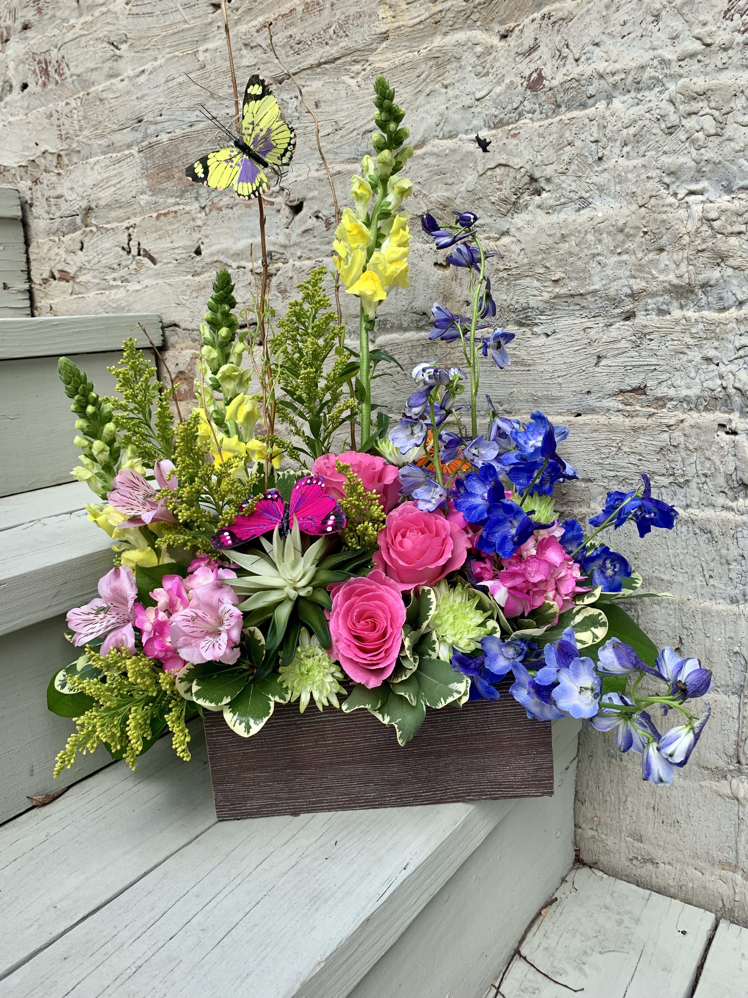 Bright mixed flower arrangement in a rectangular box with butterfly picks