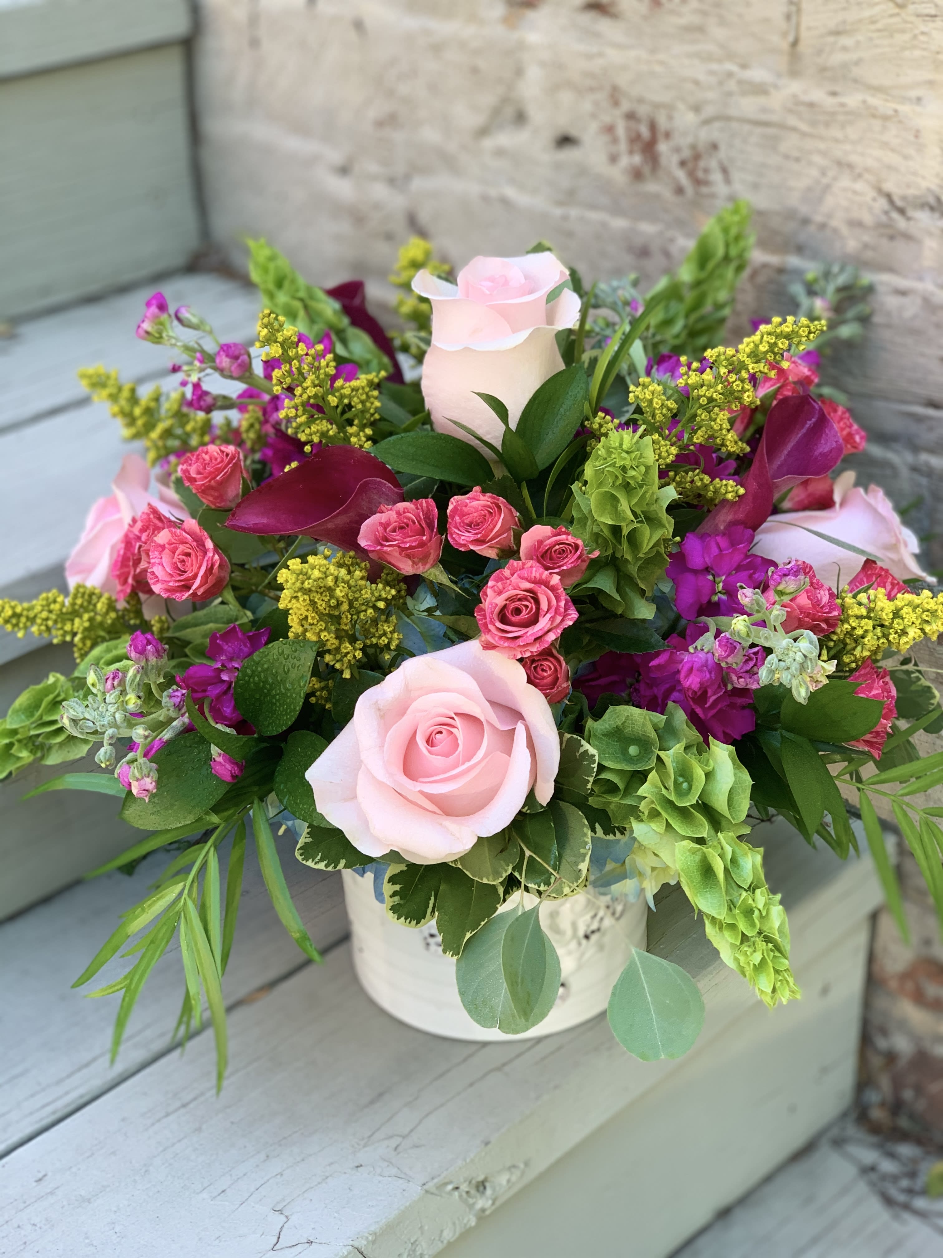 Pink roses and magenta flowers arranged in a white container