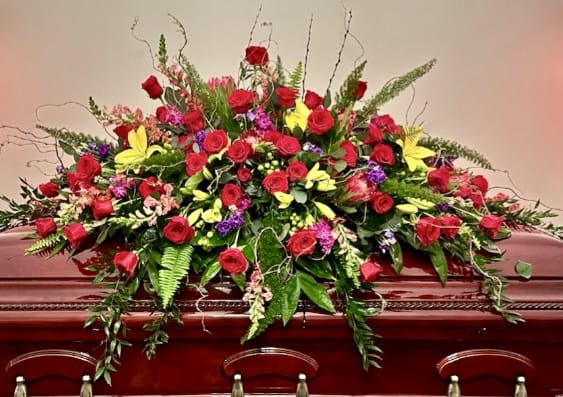 Large red and yellow floral casket spray on a wooden casket
