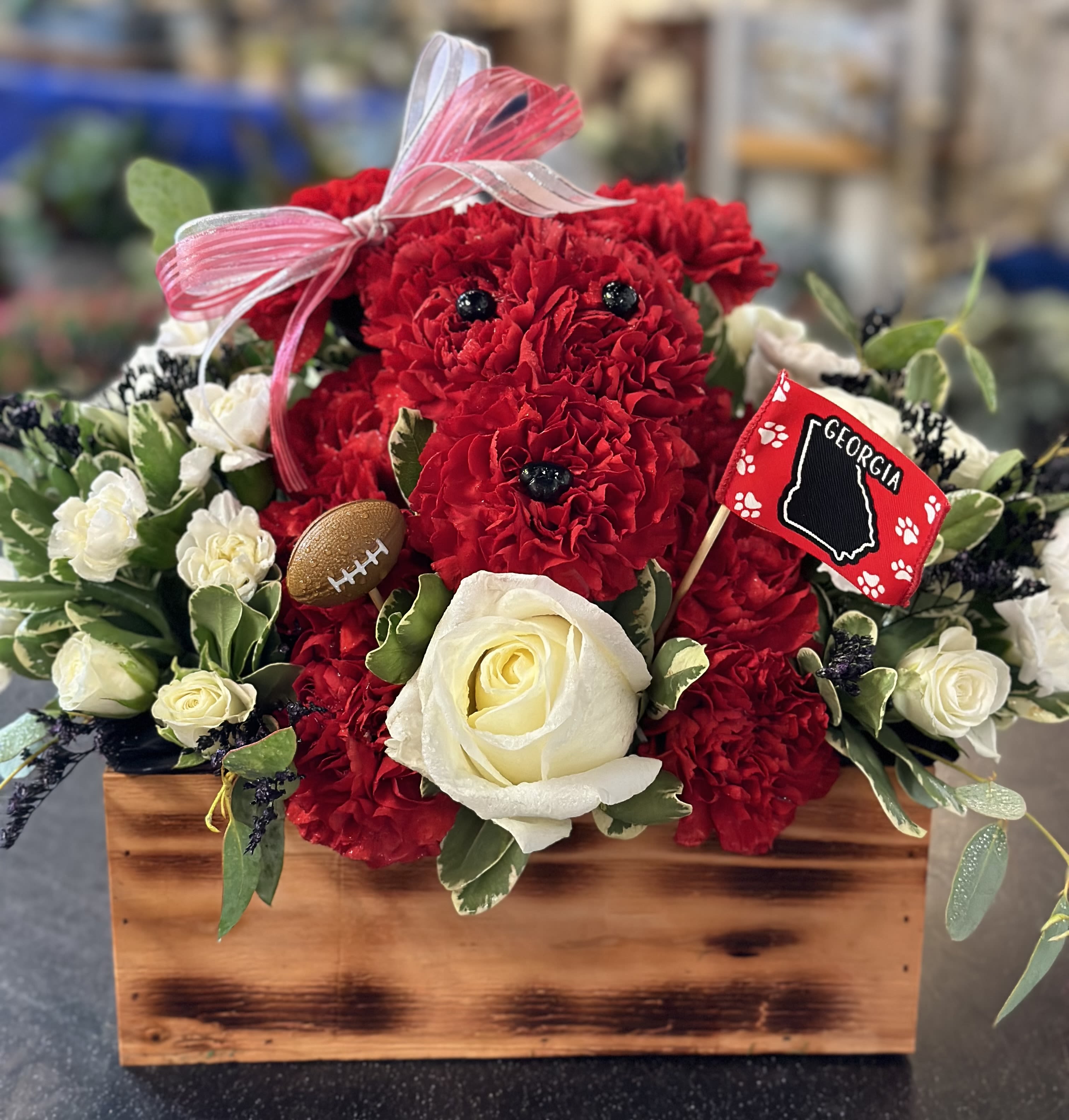 Red carnations and white roses in a wooden box with a ribbon and Georgia flag pick.