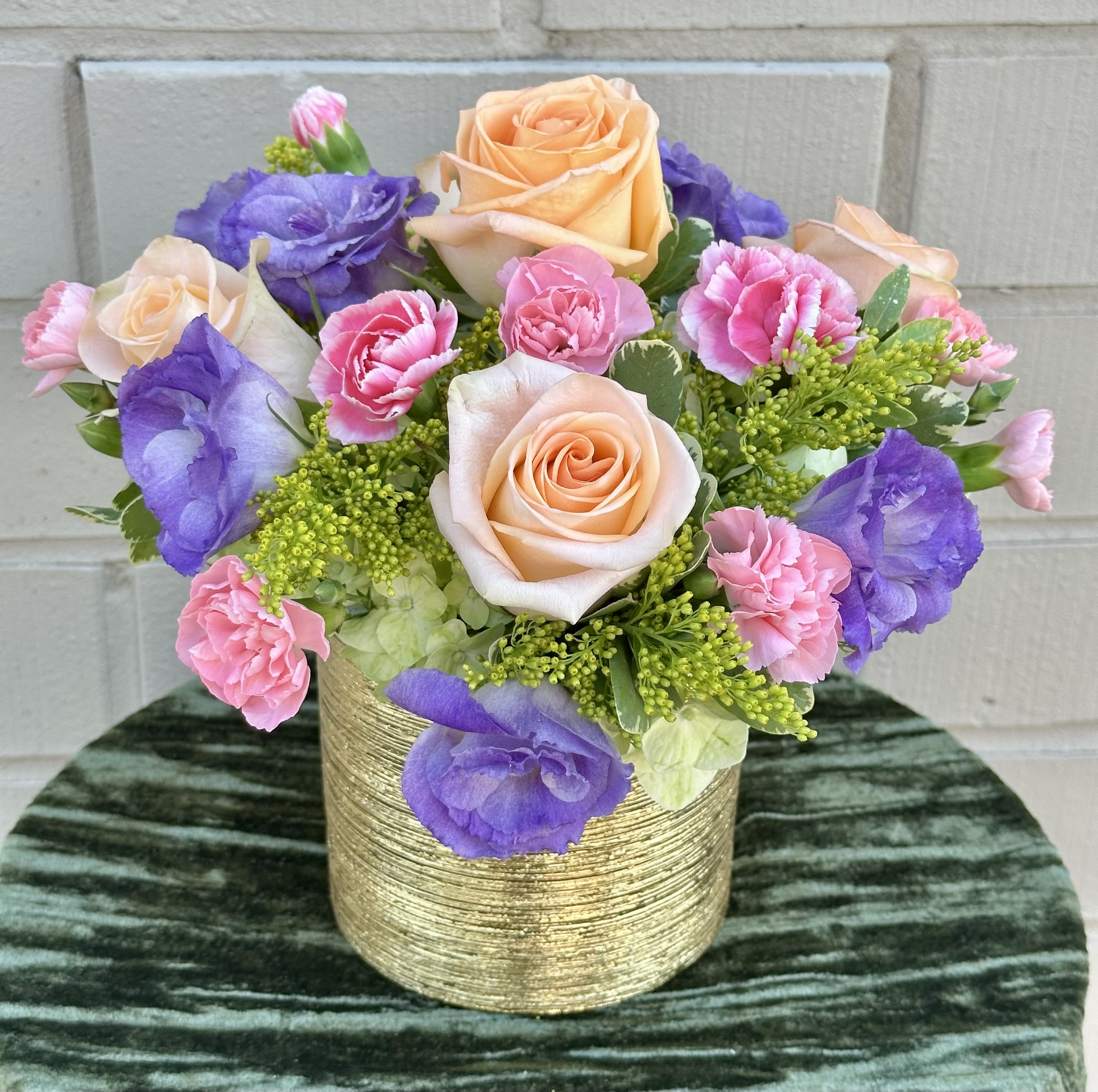 Peach roses, pink carnations, and purple lisianthus in a gold vase