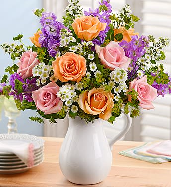 Pink and peach roses with purple flowers in a white pitcher vase