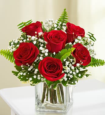 Red roses arranged in a clear square vase with white baby's breath