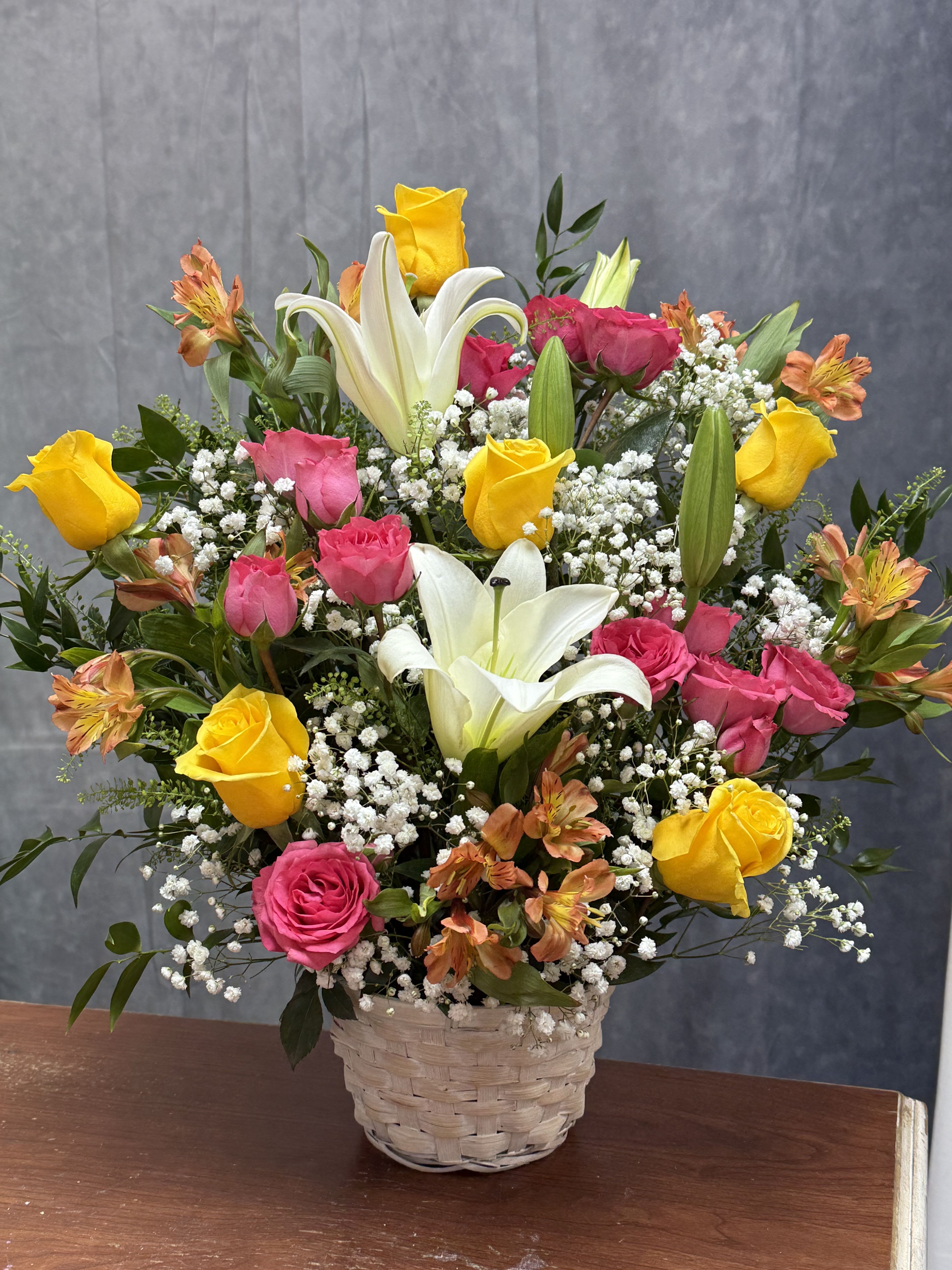 Blooming Garden basket - Bright pink, yellow and orange roses and alstroemeria with white lilies and fillers, arranged in a rustic woven basket-cheerful, celebratory blooms perfect for birthdays or everyday gifting.