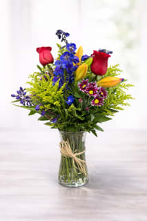 Mixed bouquet of roses, lilies, and blue flowers in a glass vase
