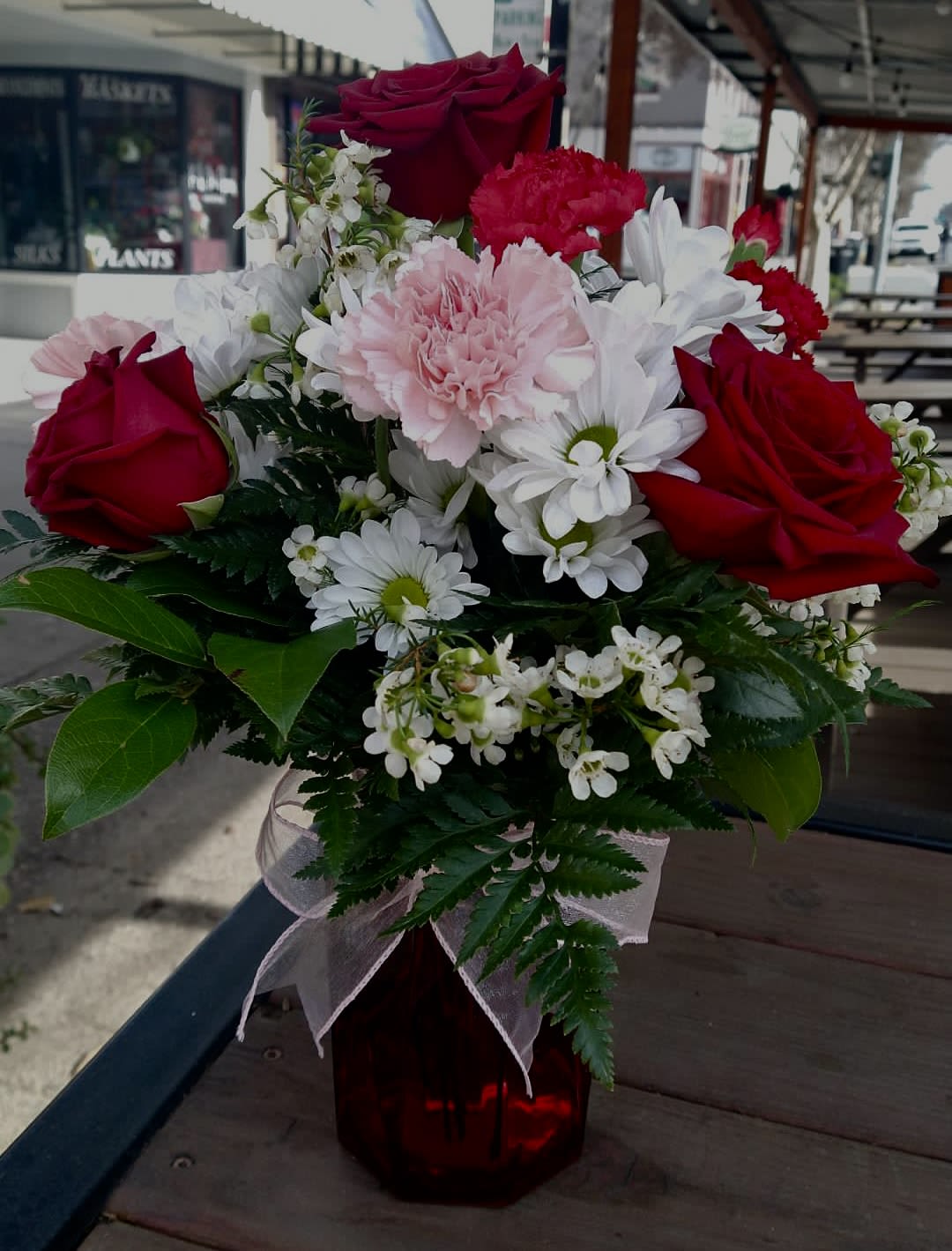 Bouquet of red roses, pink carnations, and white daisies in a red vase